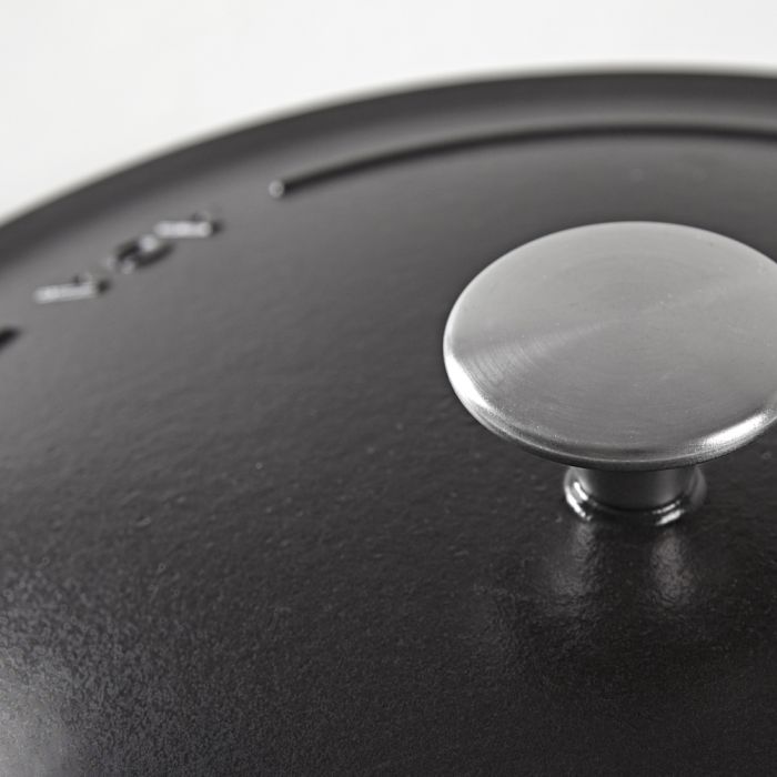 Detailaufnahme eines Topfdeckels aus Gusseisen mit Edelstahlknauf Nahaufnahme eines schwarzen Gusseisentopfdeckels mit rundem Edelstahlknauf