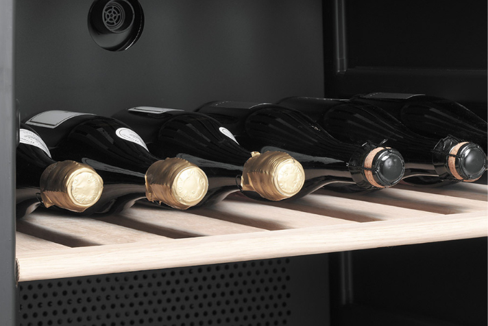 Detailansicht von Weinflaschen auf einem Holzregal in einem Weinkühlschrank Mehrere Weinflaschen mit goldenem und schwarzem Verschluss lagern waagerecht auf einem Holzregal in einem Weinkühlschrank