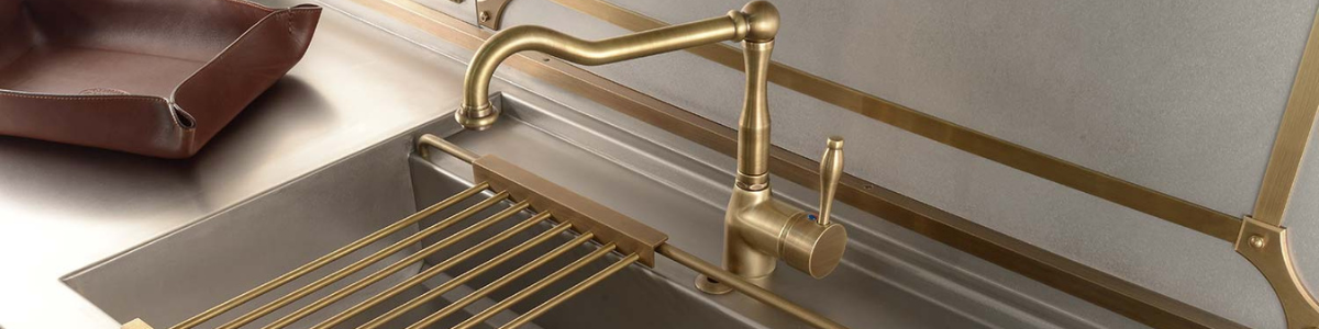 Moderne Küchenarmatur aus gebürstetem Messing mit passendem Spülbecken und Küchenzubehör Goldfarbene Küchenarmatur aus Messing an einer Edelstahlspüle mit Abtropfgitter und brauner Ablage
