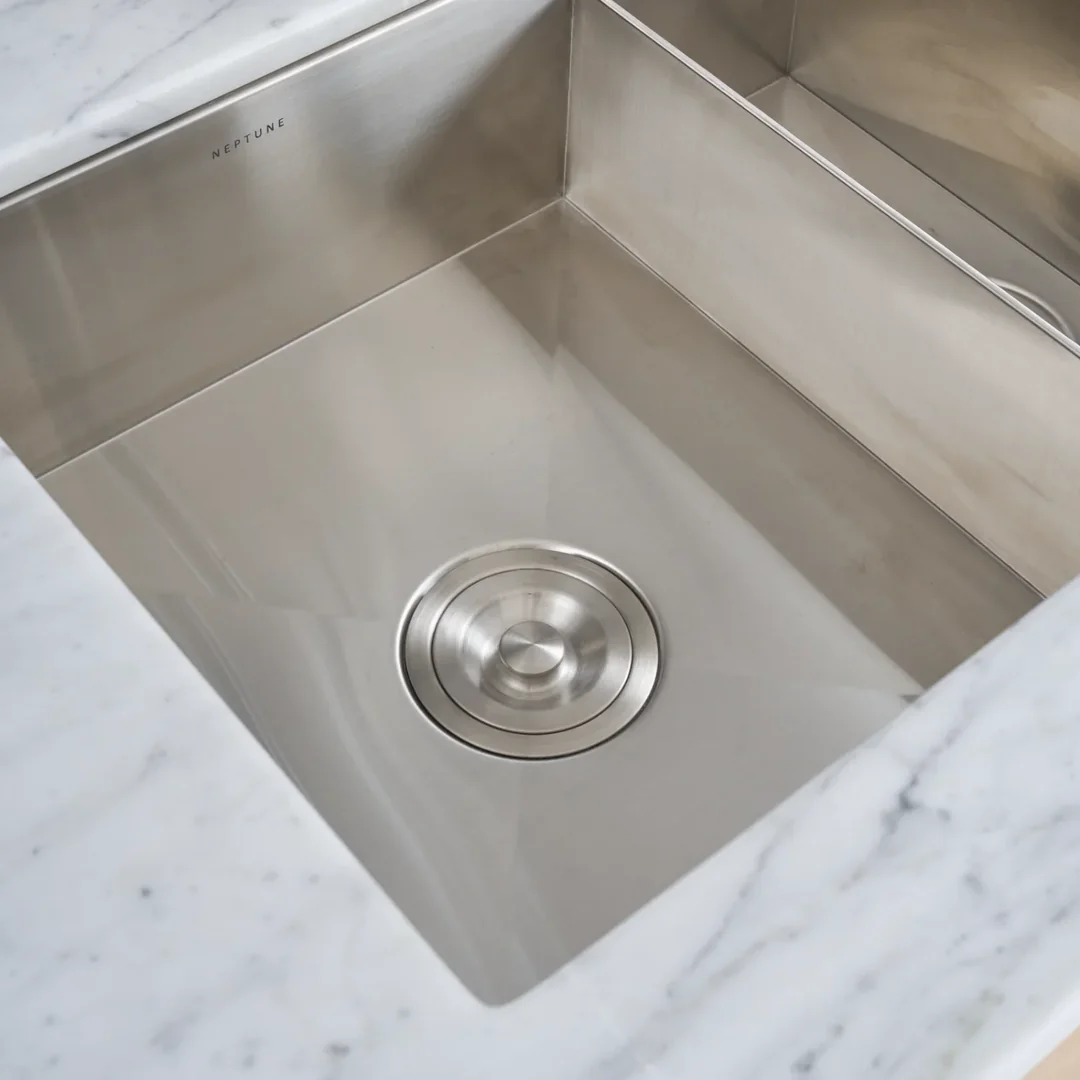 Detailansicht: rechteckiges Neptune Edelstahl-Spülbecken mit flächenbündigem Abflussdeckel in weißer Marmor-Arbeitsplatte – moderne Küchenspüle