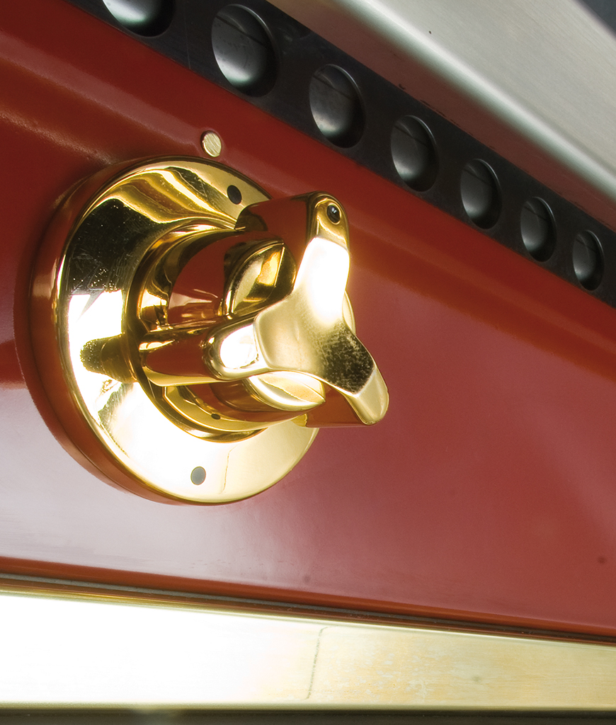 Hochwertiger goldfarbener Drehknauf auf roter Metalloberfläche Goldener Drehknauf an einem roten Haushaltsgerät, Nahaufnahme mit edler Optik
