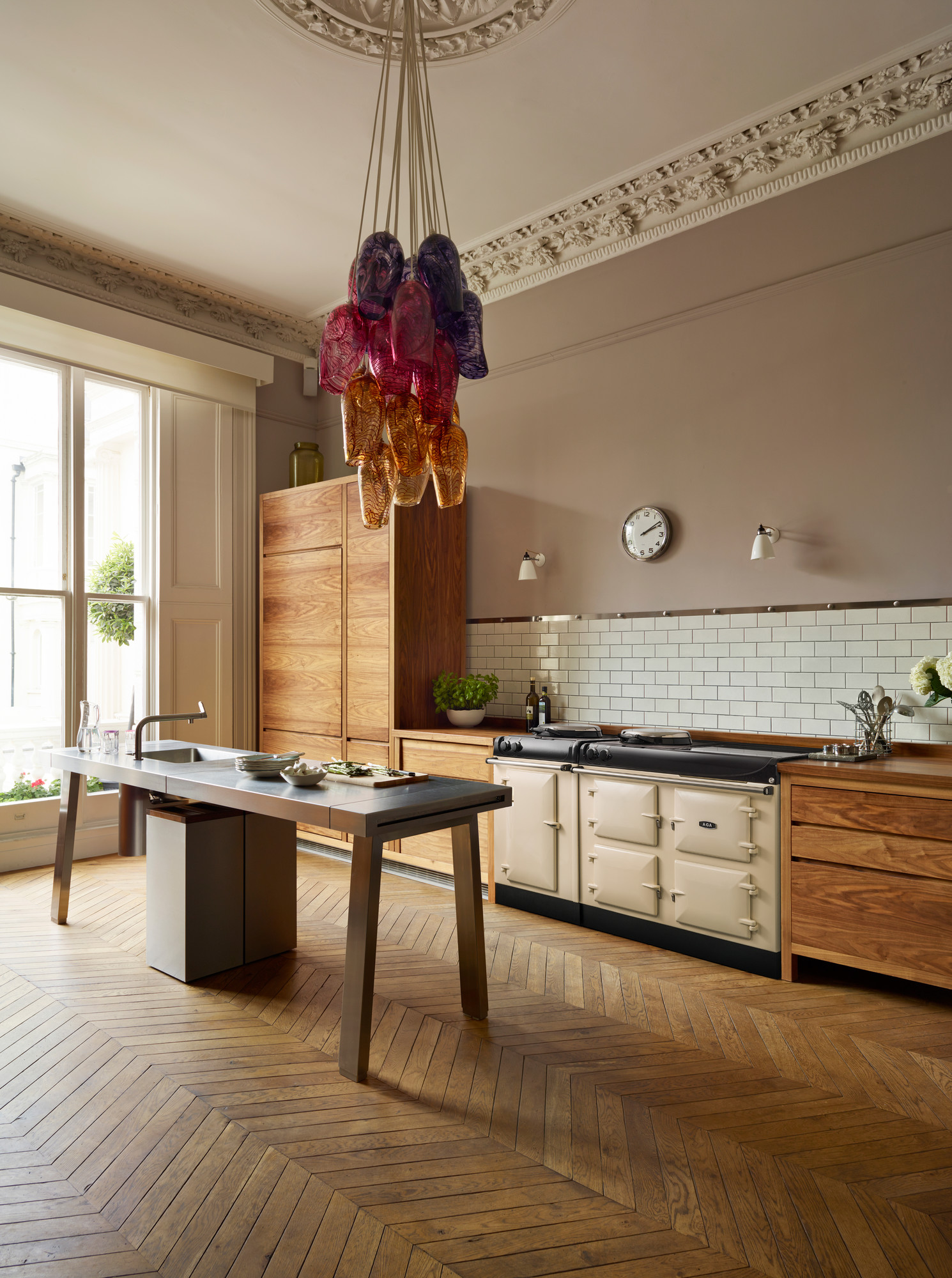 Moderne Küche mit Holzmöbeln, Designerlampe und großem Fenster Helle, moderne Küche mit eleganten Holzmöbeln, großem Induktionsherd, Designer-Pendelleuchte aus buntem Glas und Parkettboden