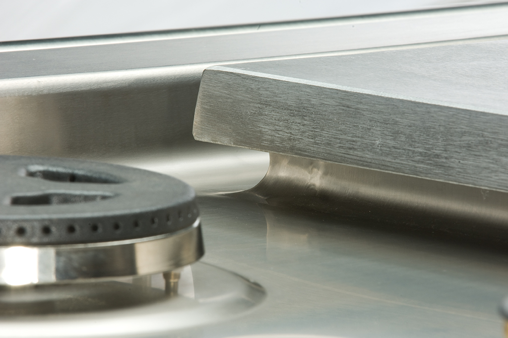 Detailansicht eines Gasherds aus Edelstahl mit Brenner und robustem Kochfeldrand Nahaufnahme eines modernen Gasherds aus Edelstahl mit sichtbarem Brenner und sauber verarbeitetem Übergang am Kochfeldrand