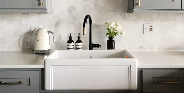 Moderne Küchenzeile mit weißer Keramikspüle, schwarzer Armatur und grauen Schränken Stilvolle Küche mit weißer Keramikspüle, schwarzer Armatur, grauen Schränken, einem Wasserkocher und Deko-Accessoires auf der Arbeitsfläche