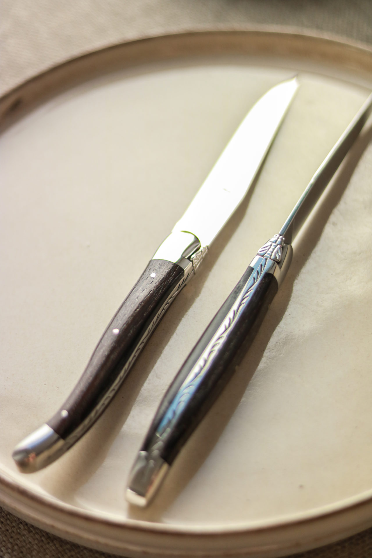 Elegantes Steakmesser-Set mit dunklem Holzgriff auf cremefarbenem Teller Zwei hochwertige Steakmesser mit dunklem Holzgriff und verziertem Metall auf einem hellen Teller