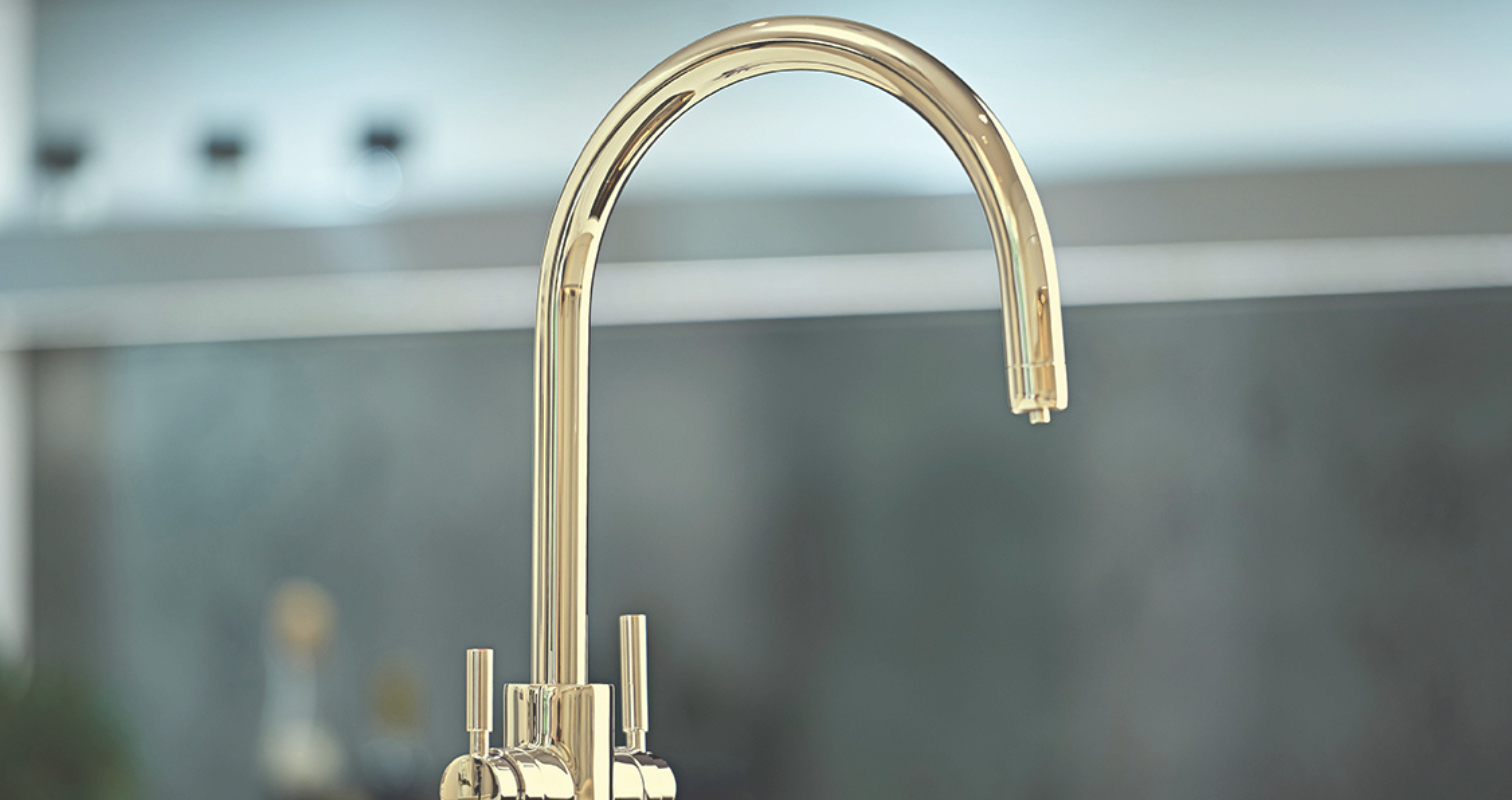 Elegante goldene Küchenarmatur mit modernem Design Goldene Küchenarmatur mit gebogenem Auslauf und zwei Hebeln in moderner Küche