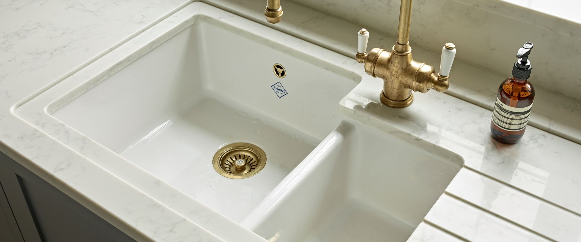 Weiße Keramik-Küchenspüle mit zwei Becken, Ablaufgarnitur in Messing, passender Retro-Armatur und Abtropffläche auf Marmorarbeitsplatte – hochwertiges Spülen-Set für die Küche