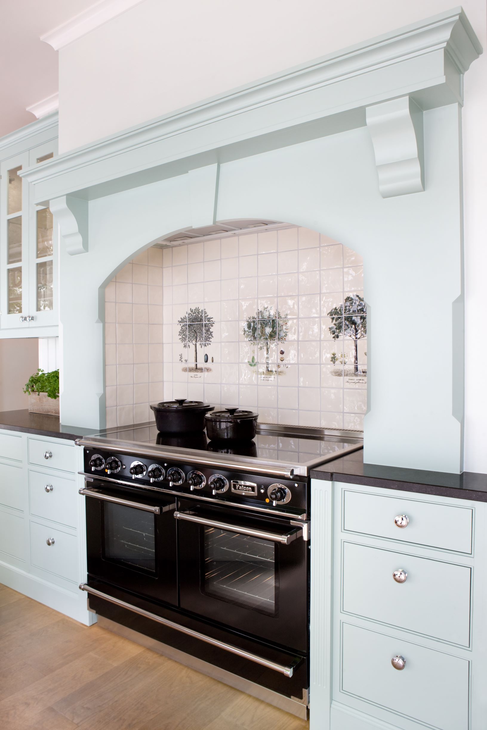 Herd und Backofen im Landhausstil mit hellblauer Küchenzeile und Fliesenspiegel mit Baum-Motiven Moderner schwarzer Herd mit zwei Backöfen, umgeben von hellblauen Küchenschränken und dekorativem Fliesenspiegel mit Baum-Abbildungen
