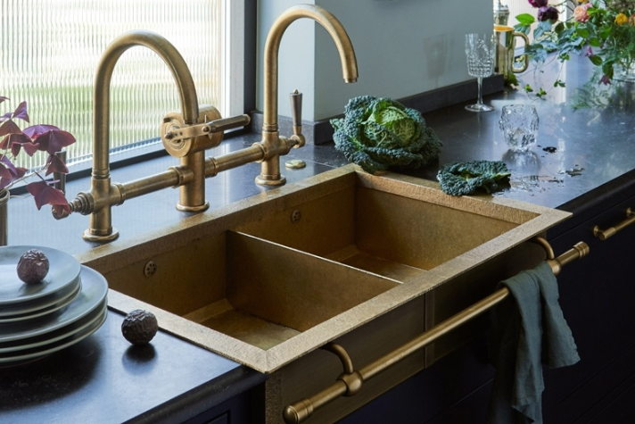 Luxuriöses Spülbecken aus Messing mit passender Armatur in moderner Küche Doppeltes Spülbecken aus Messing mit goldener Armatur, Gemüse und Geschirr auf schwarzer Arbeitsplatte in stilvoller Küche