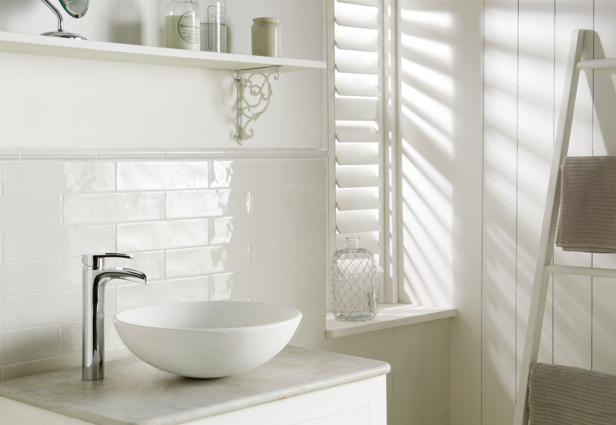 Modernes weißes Badezimmer mit Waschbecken, Armatur und stilvollen Deko-Elementen Helles, modernes Badezimmer mit rundem Aufsatzwaschbecken, verchromter Armatur, weißen Wandfliesen, Deko-Gegenständen und gestapelten Handtüchern auf einer Leiter