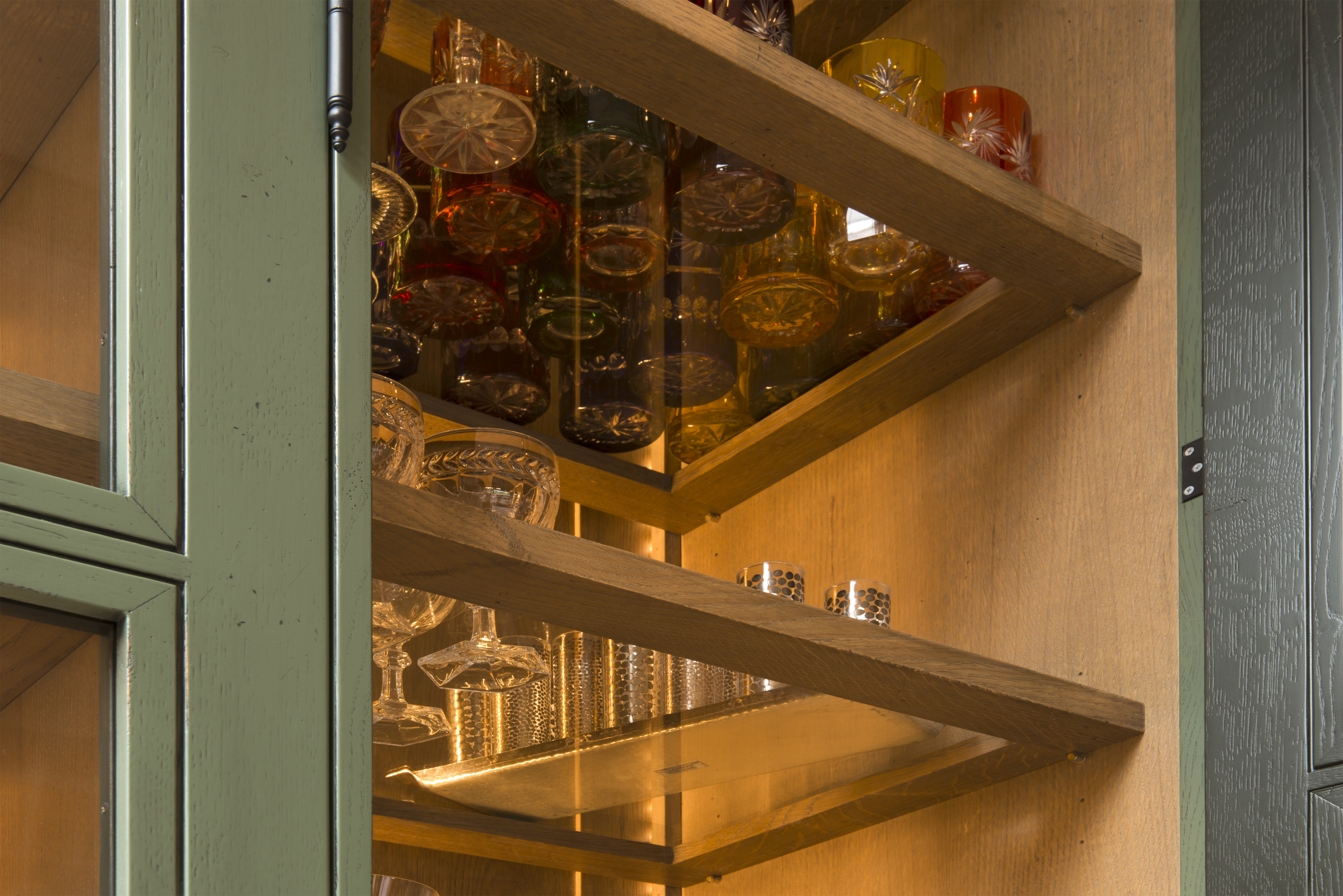 Offener grüner Holzschrank mit Gläsern und Kristallgläsern auf Regalbrettern, warm beleuchtet