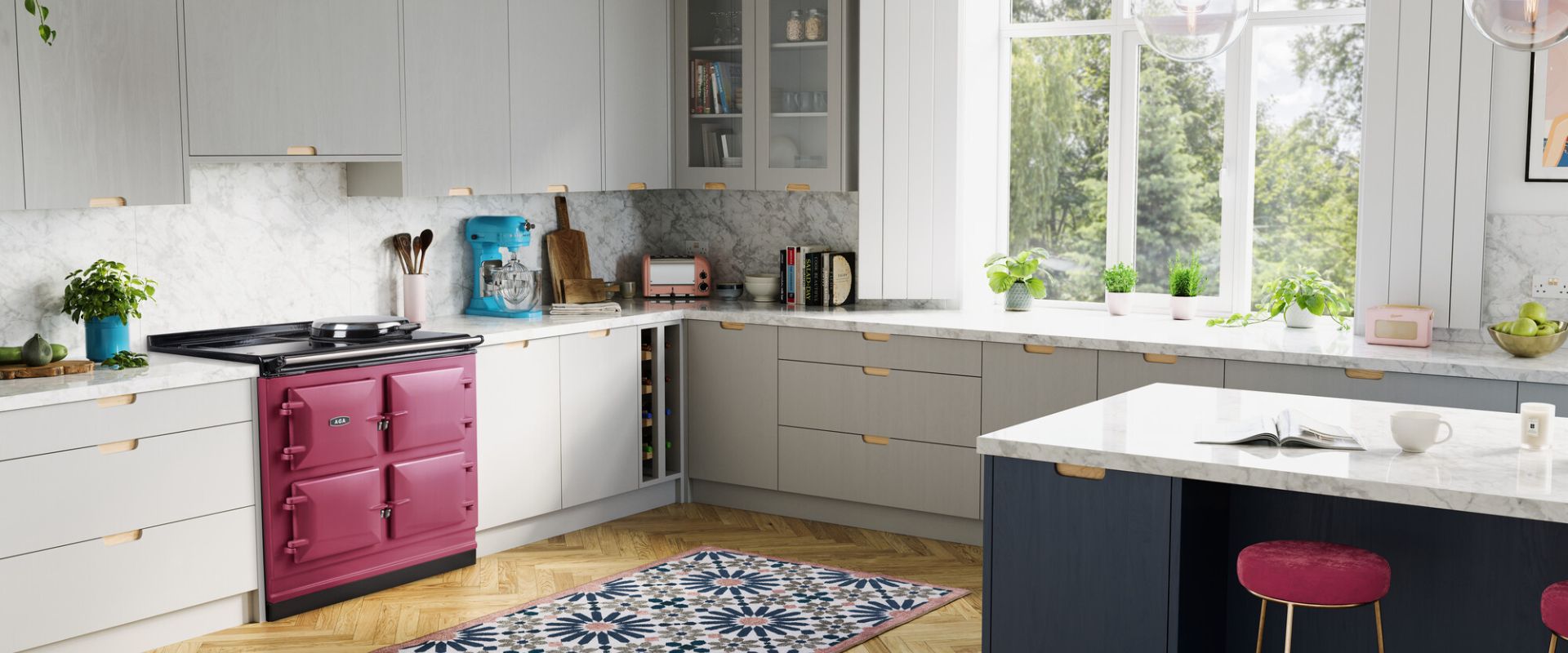 Helle Designküche im L-Format mit Kochinsel, grauen Schränken, Marmor-Optik Arbeitsplatte, pinkem Range Cooker, blauem Standmixer und pastellfarbenen Akzenten – ideal für stilvolles Kochen