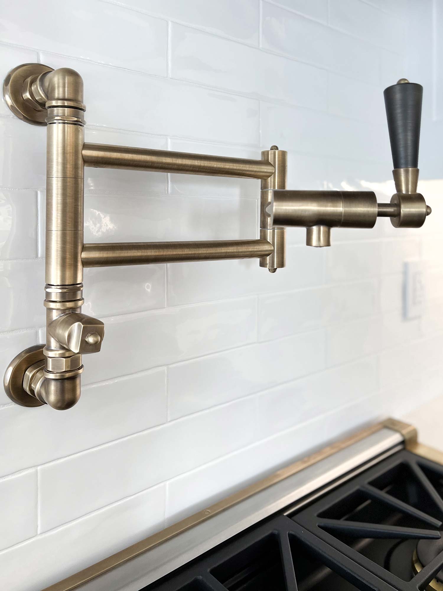 Wandmontierter Topffüller aus Messing für die Küche Schwenkbarer Topffüller aus gebürstetem Messing, an einer weißen Küchenwand über einem Herd montiert