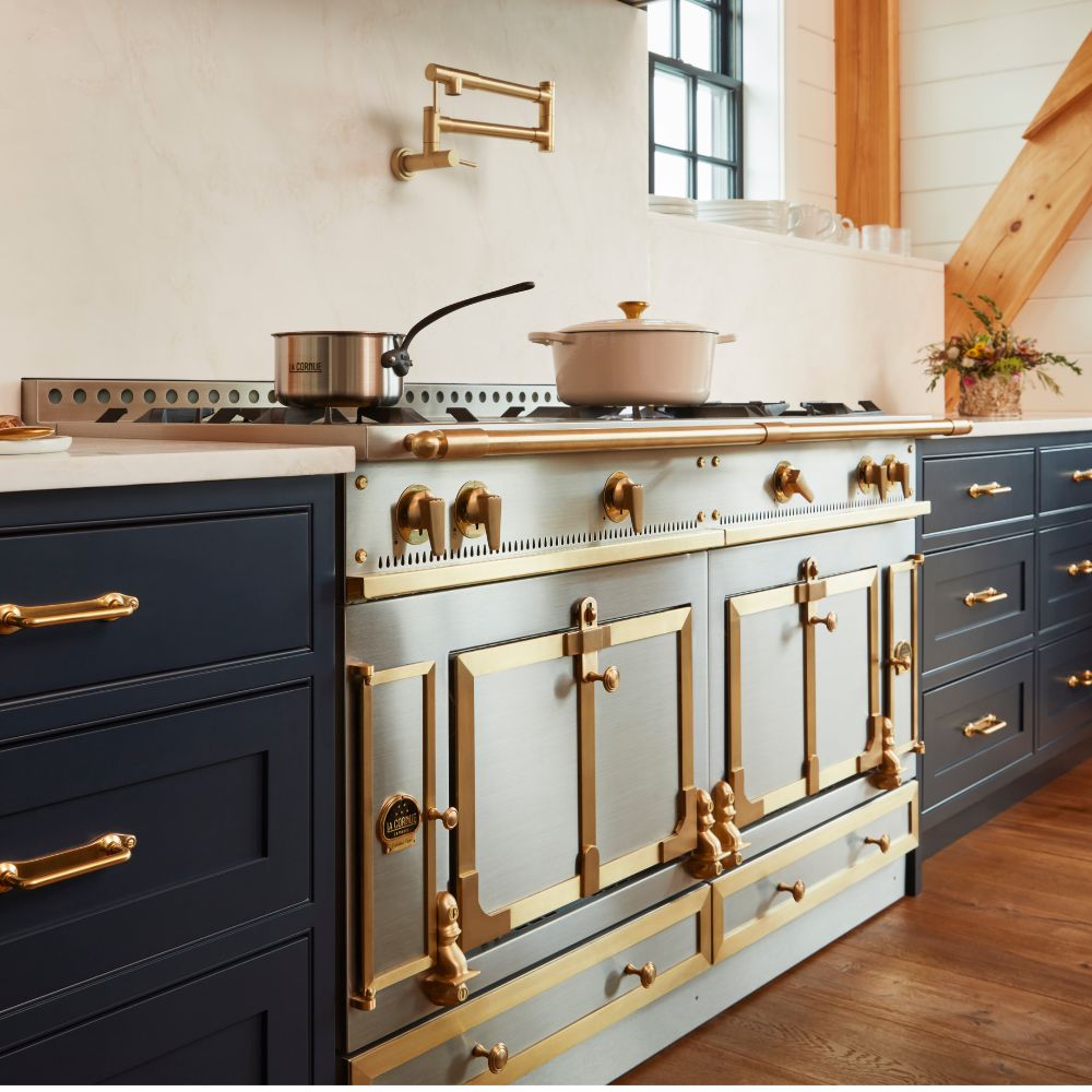 Hochwertiger Standherd aus Edelstahl mit goldenen Messinggriffen, Gasbrennern und großem Backofen, integriert in moderne Küche mit dunkelblauen Schränken – ideal für anspruchsvolles Kochen.