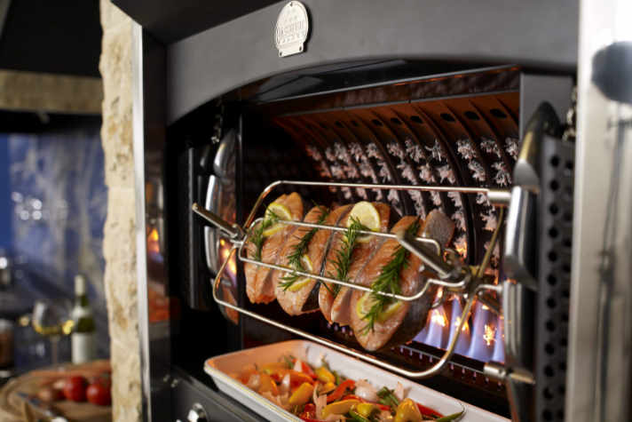 Fischfilets mit Zitronenscheiben und Rosmarin im Grillofen, darunter eine Schale mit frischem Ofengemüse Frische Fischfilets mit Zitronen und Rosmarin werden im hochwertigen Grillofen gegrillt, darunter befindet sich buntes Ofengemüse in einer Form