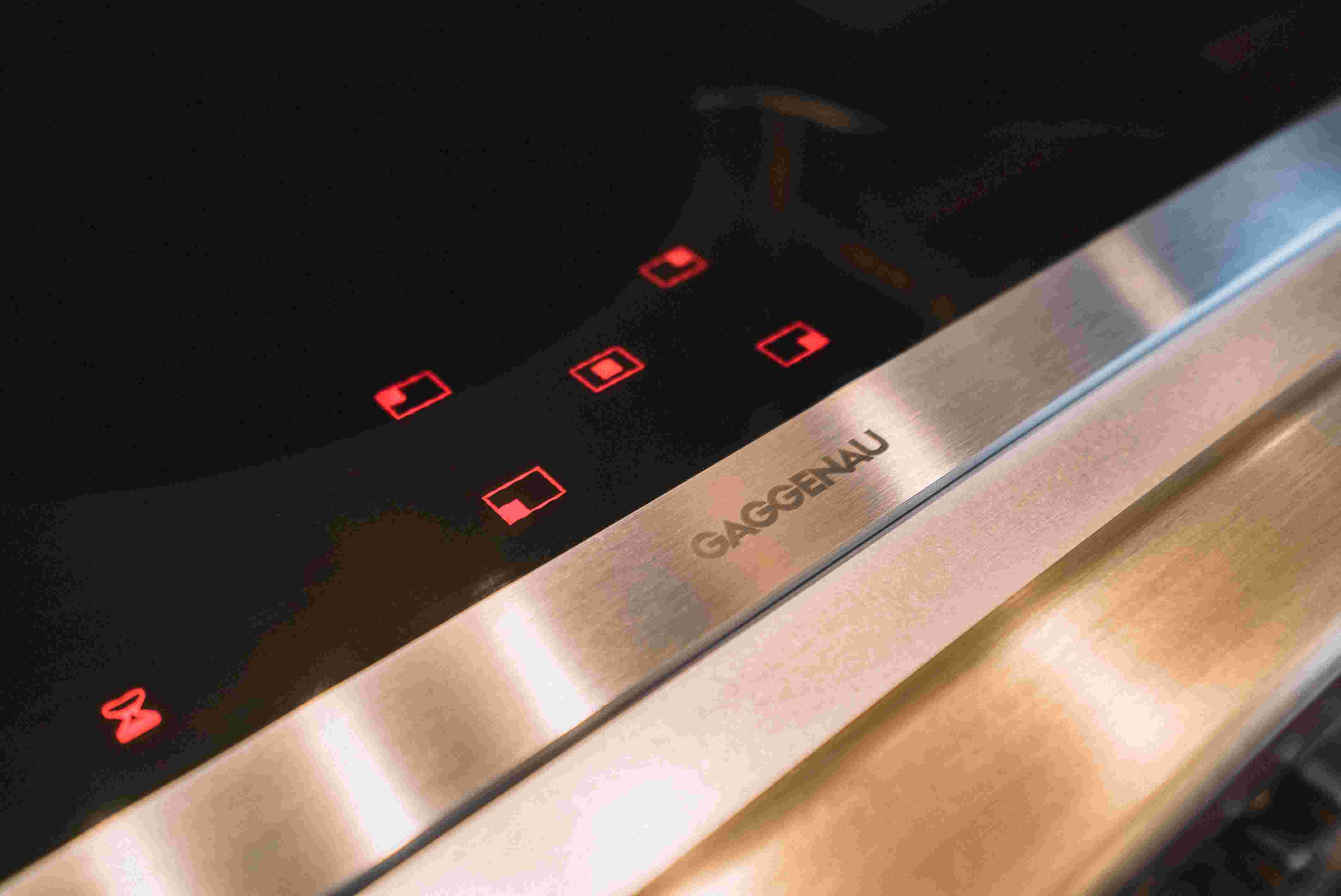 Nahaufnahme eines Gaggenau Induktionskochfelds mit leuchtenden roten Touch-Symbolen und Edelstahlverkleidung