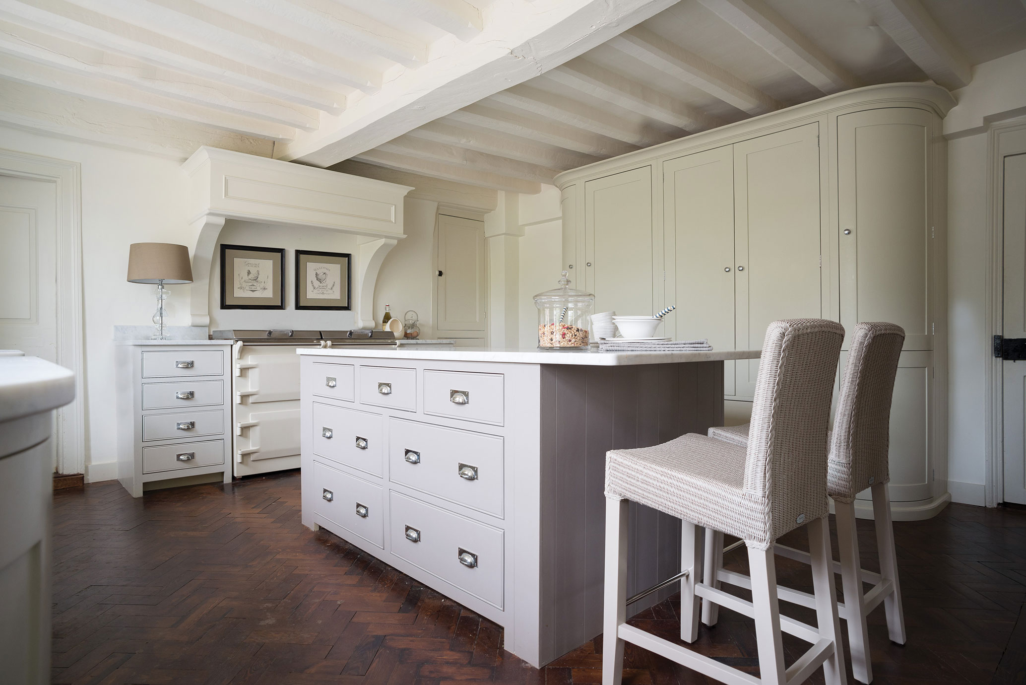 Elegante Landhausküche in Cremeweiß mit Kücheninsel und modernen Barhockern Helle, stilvolle Landhausküche mit cremeweißen Möbeln, Kücheninsel, Barhockern und Holzfußboden