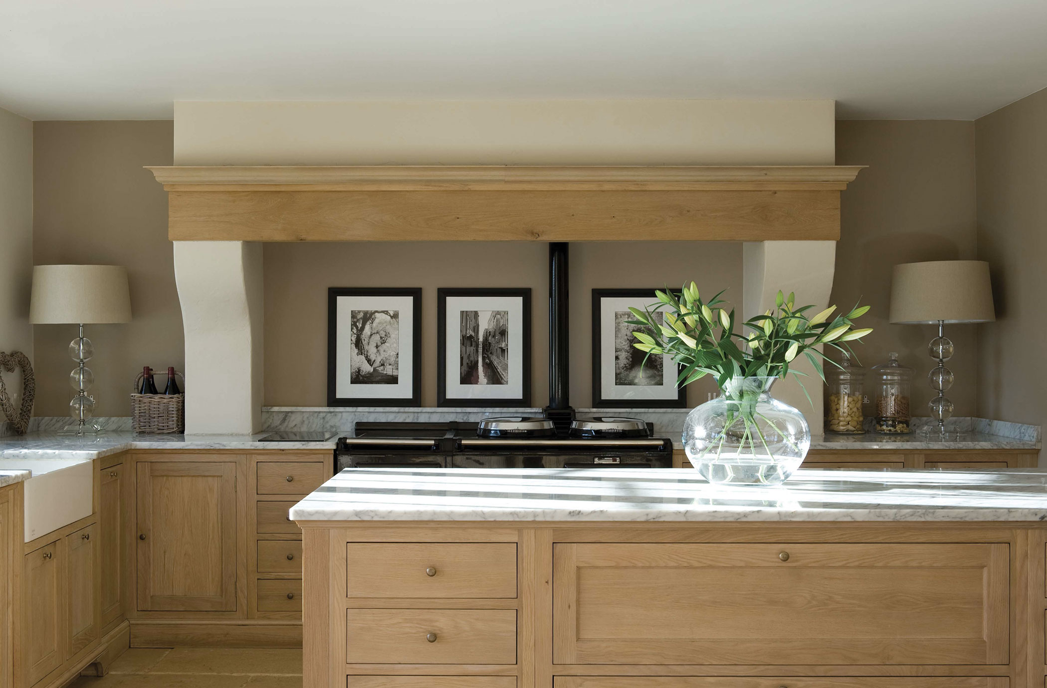 Moderne Landhausküche mit Holzfronten und Marmorarbeitsplatten, stilvoll dekoriert Helle Landhausküche mit Holzfronten, Marmorarbeitsflächen, einem Glasvase mit frischen Blumen und dekorativen Elementen auf den Arbeitsplatten