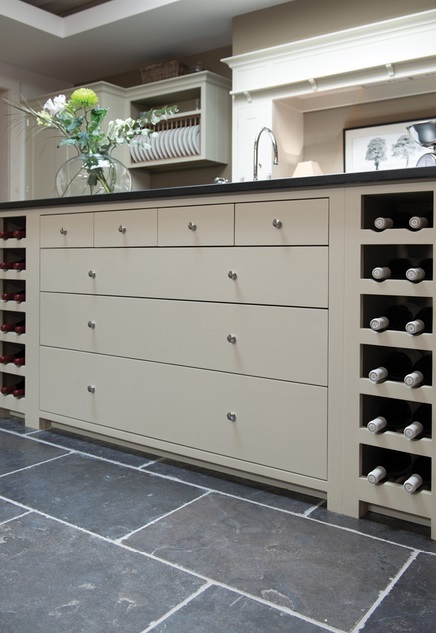Moderne Kücheninsel mit Weinregalen und Schubladen in cremefarbenem Design Kücheninsel mit integrierten Weinregalen, mehreren Schubladen und grauer Arbeitsplatte auf Steinfliesenboden