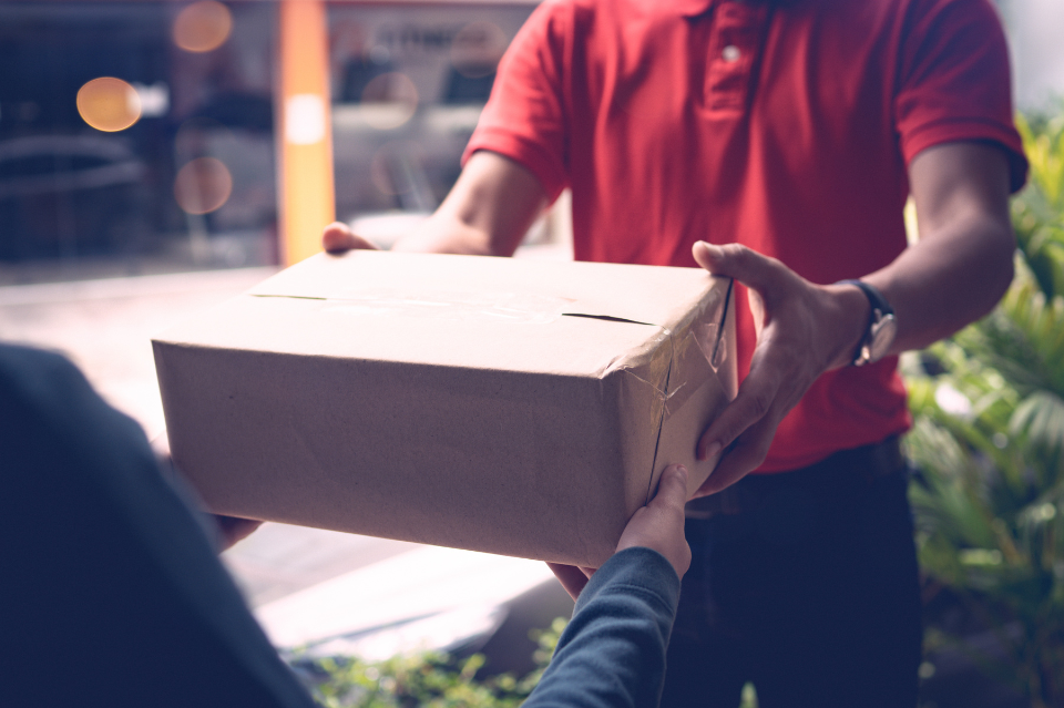Eine Person in rotem Shirt überreicht einer anderen Person ein Paket an der Tür