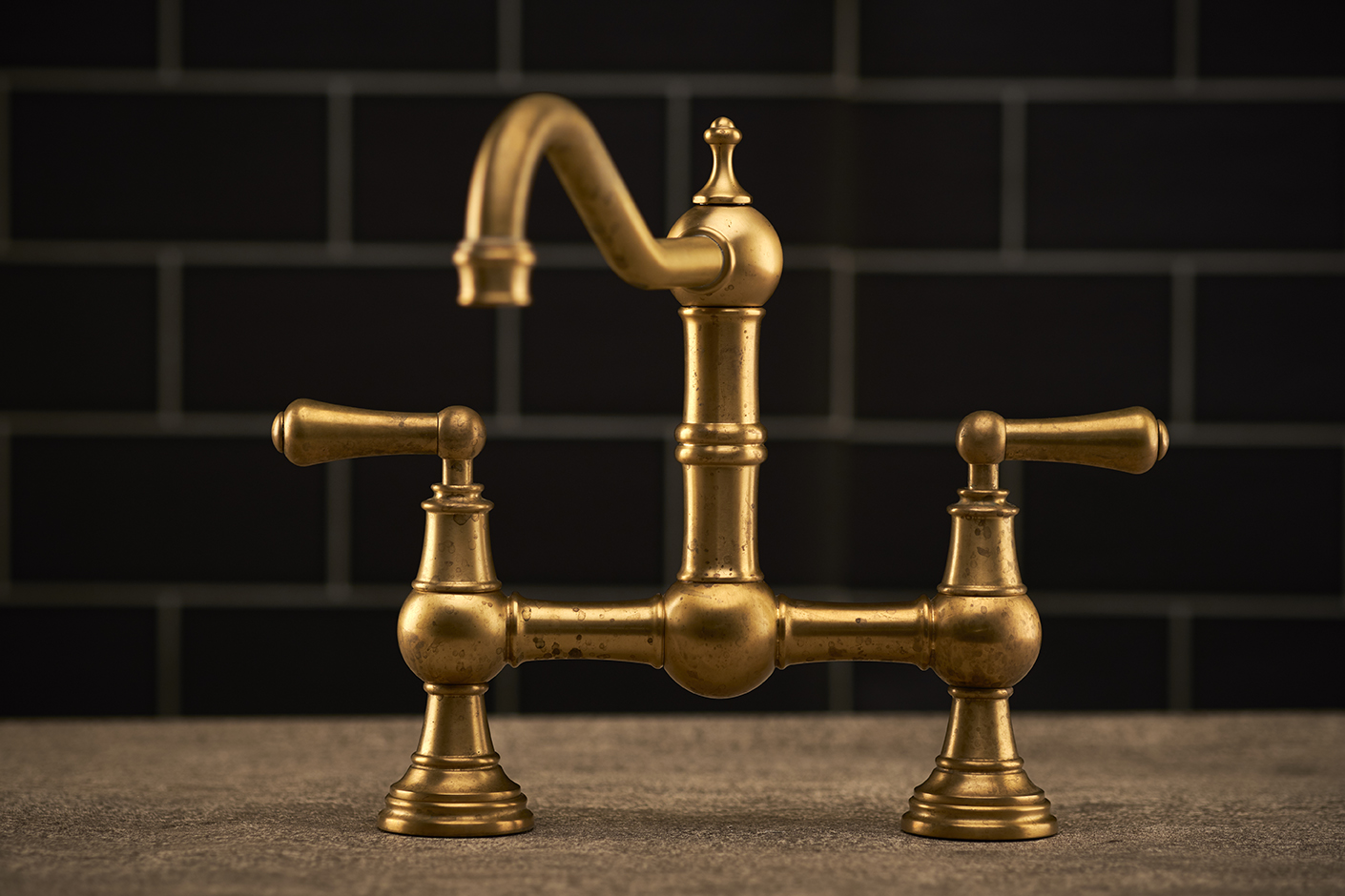 Detailaufnahme einer klassischen Armatur aus Messing mit zwei Drehgriffen vor schwarzem Fliesenspiegel