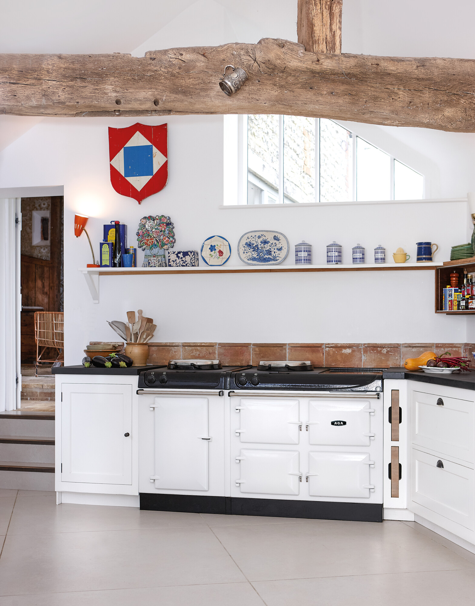 Moderne Landhausküche mit weißem AGA-Herd und stilvollen Deko-Elementen Helle, moderne Landhausküche mit weißem AGA-Herd, rustikalen Holzbalken und dekorativem Regal mit Teller- und Dosenarrangement