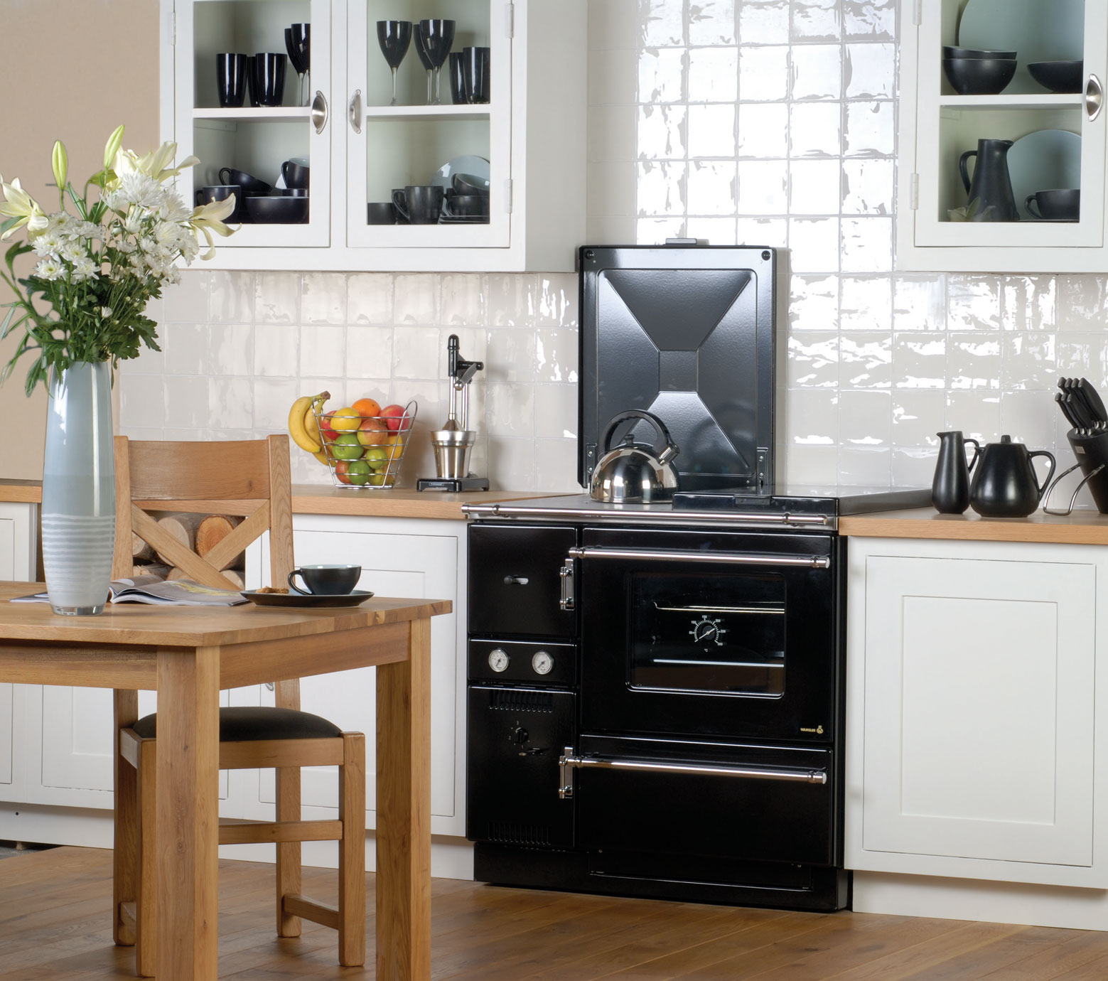 Moderne Landhausküche mit Holzofen, Esstisch und stilvoller Einrichtung Helle Landhausküche mit schwarzem Holzofen, Esstisch aus Holz, Blumen in Vase, Obstschale und Küchenzubehör