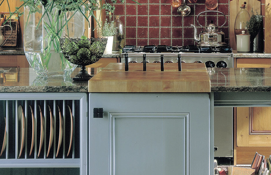 Moderne Landhausküche mit Messerblock, Gasherd und stilvoller Arbeitsplatte aus Granit Detailansicht einer modernen Küche mit Granit-Arbeitsplatte, Messerblock, Gasherd, Deko-Schale und großen Glasvasen mit Blumen