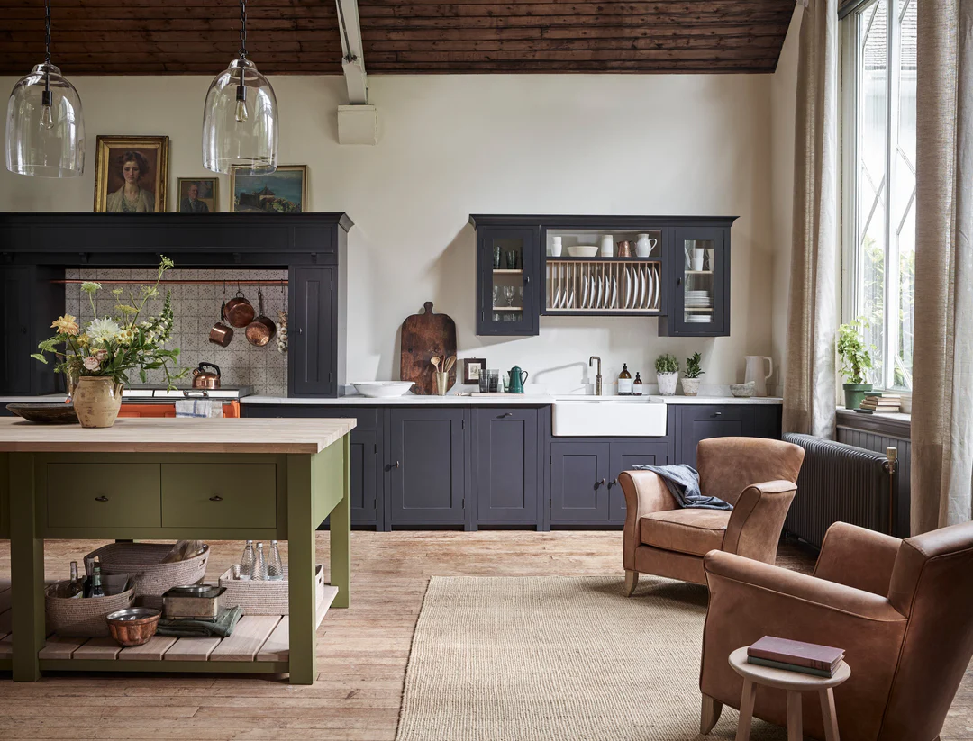 Gemütliche Landhausküche mit dunkelgrauen Einbauten, offener Tellerablage, Keramikspüle und grüner Holz-Kücheninsel; plus zwei Leder-Sessel – zeigt stilvolle Küchenmöbel und Aufbewahrungslösungen