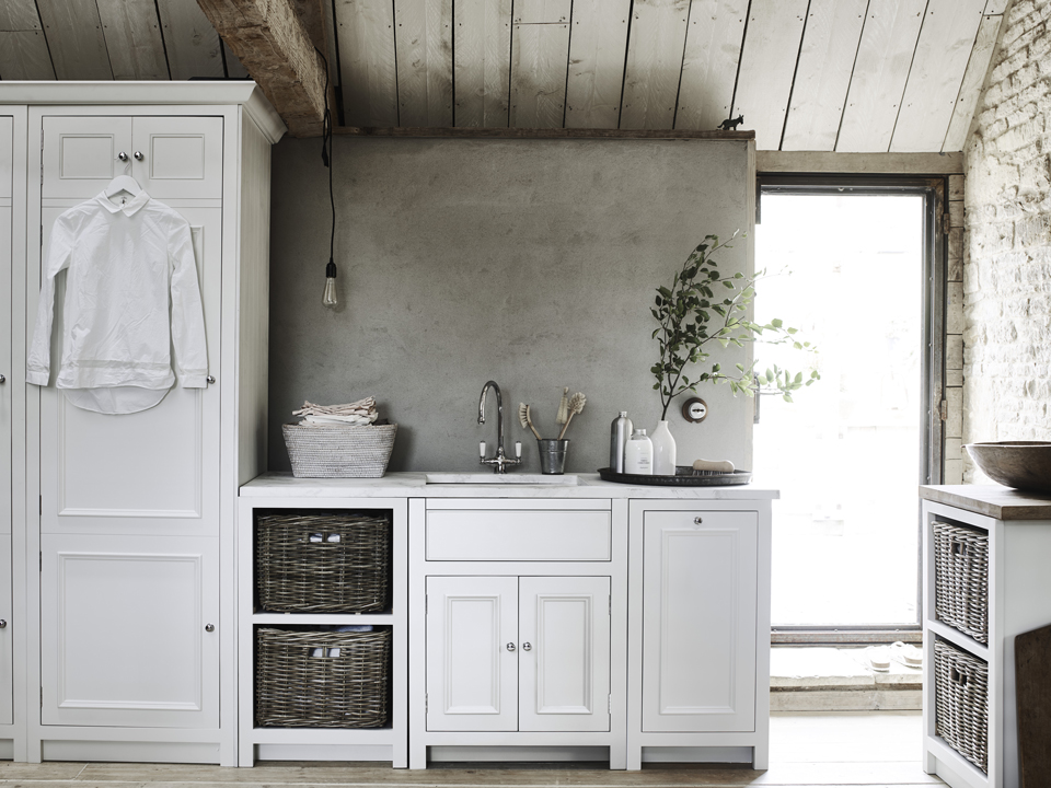 Helle Landhausküche mit weißen Schränken, offenen Körben und rustikalem Charme Moderne Landhausküche mit weißen Holzmöbeln, Natursteinwand, geflochtenen Körben und Spüle, dekoriert mit Pflanzen und Geschirr