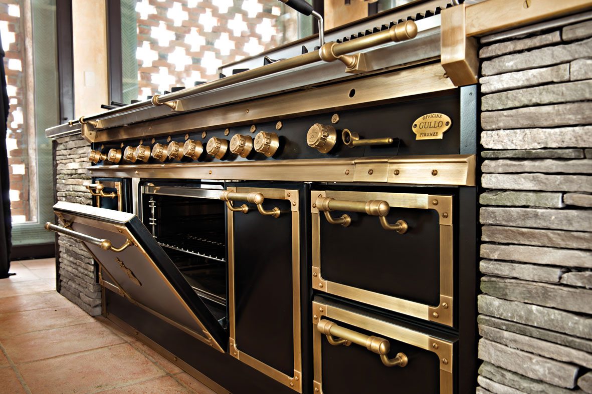 Hochwertiger Officine Gullo Herd mit goldfarbenen Details, offenem Backofen und Steinwand in stilvoller Küche