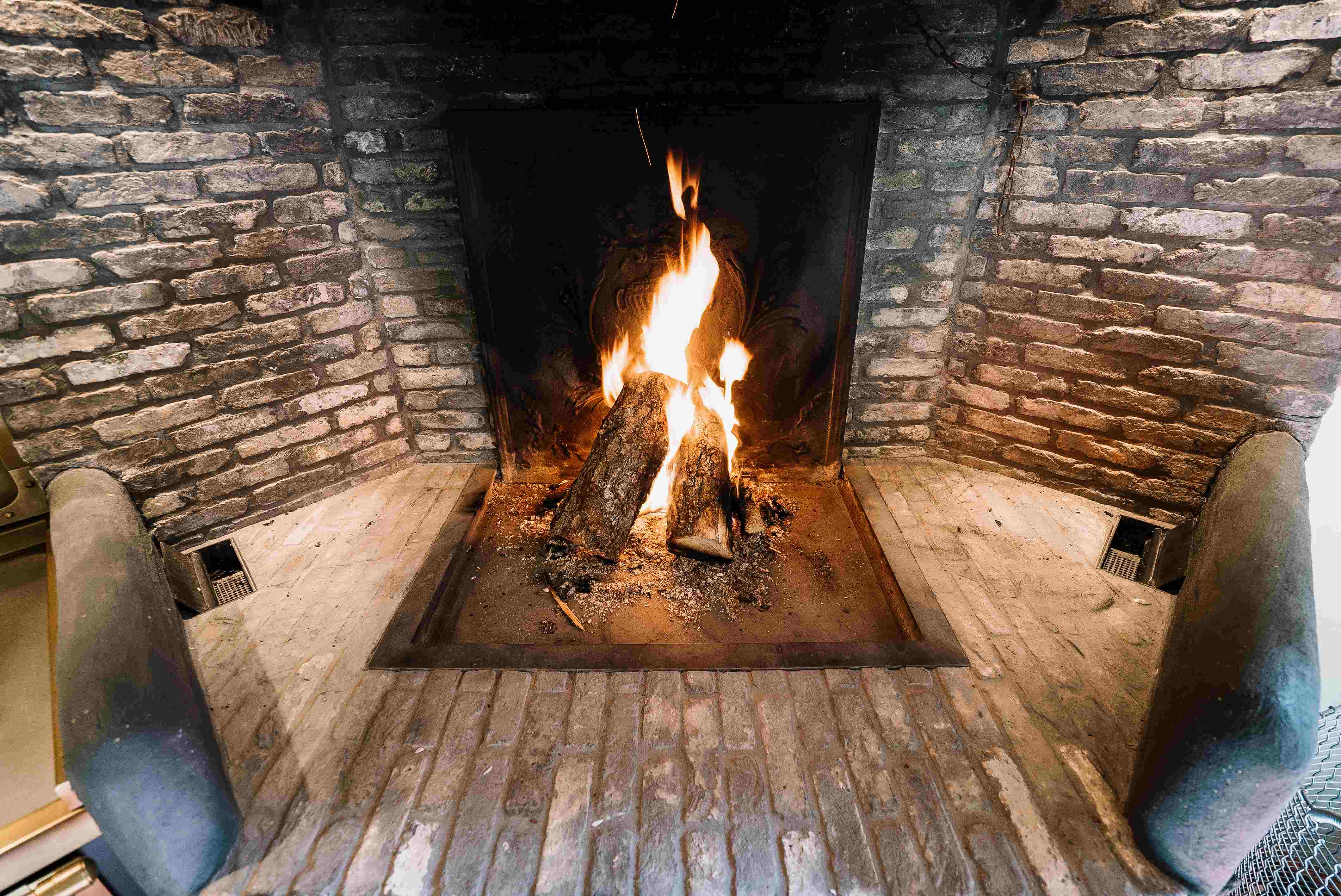 Ein offener Kamin aus Backstein, in dem zwei Holzscheite brennen und ein warmes Feuer lodert