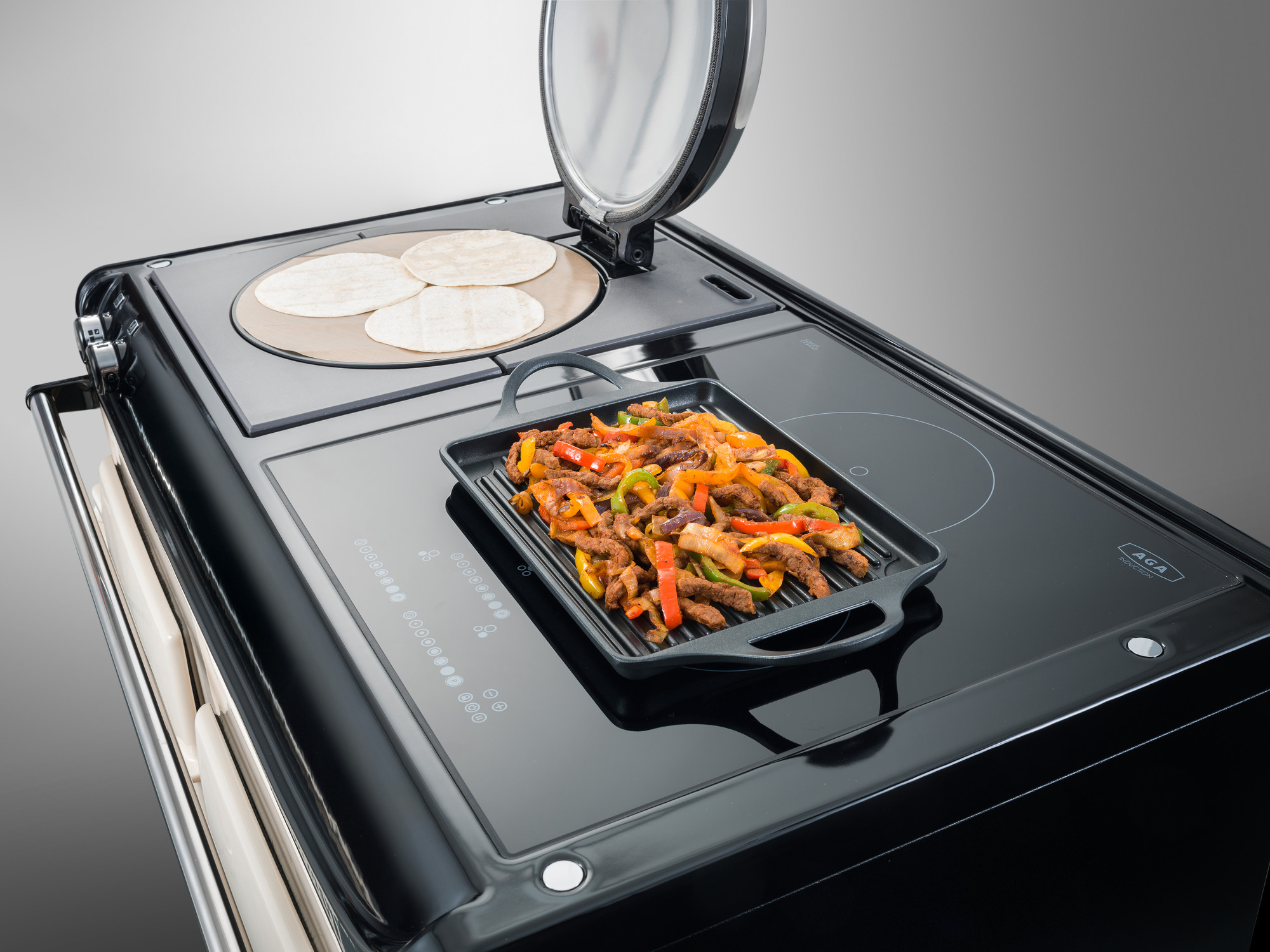Moderner Herd mit Grillplatte und warmen Tortillas auf Kochfeld Schwarzer Herd mit Grillplatte, darauf gebratene Fleischstreifen mit Paprika, und nebenbei Tortillas auf einem separaten Kochfeld