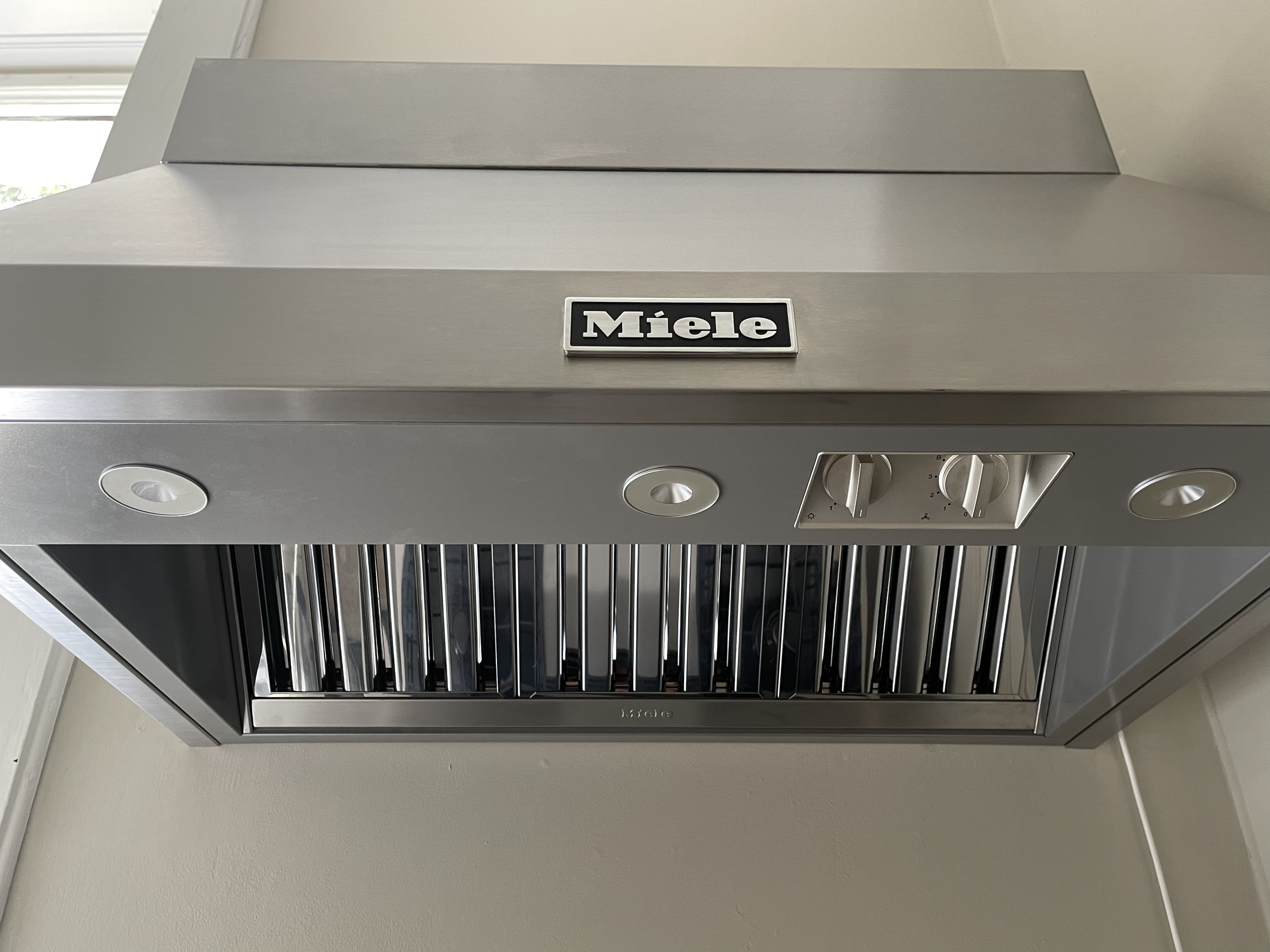 Edelstahl Dunstabzugshaube von Miele mit Kontrollknöpfen und Beleuchtung, montiert an einer Küchenwand