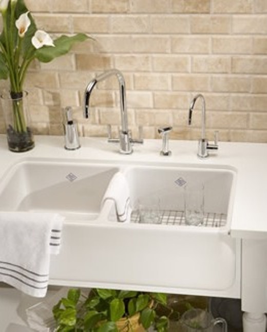 Moderne Küchenspüle mit zwei Becken und Armaturen aus Edelstahl vor Ziegelwand Weiße Doppelspüle mit verchromten Wasserhähnen, Handtuch, Gläsern und Vase vor beige Ziegelwand in moderner Küche