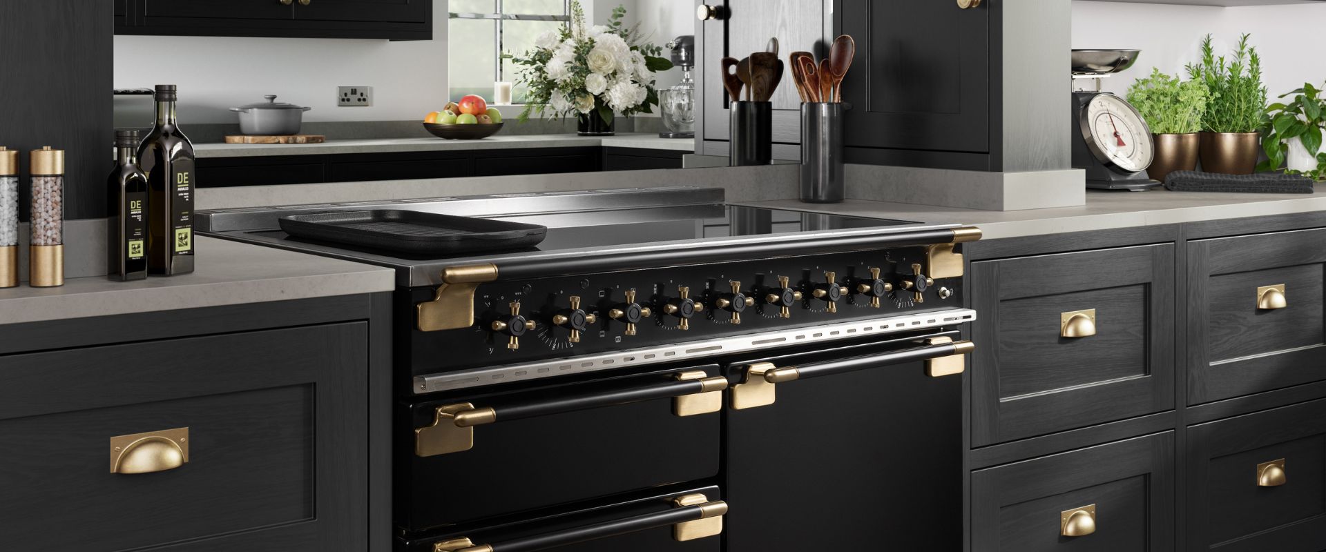 Schwarzer Standherd (Range Cooker) mit Induktionskochfeld, vielen Reglern und Messing-Beschlägen in dunkler Designküche – ideal für anspruchsvolles Kochen und Backen