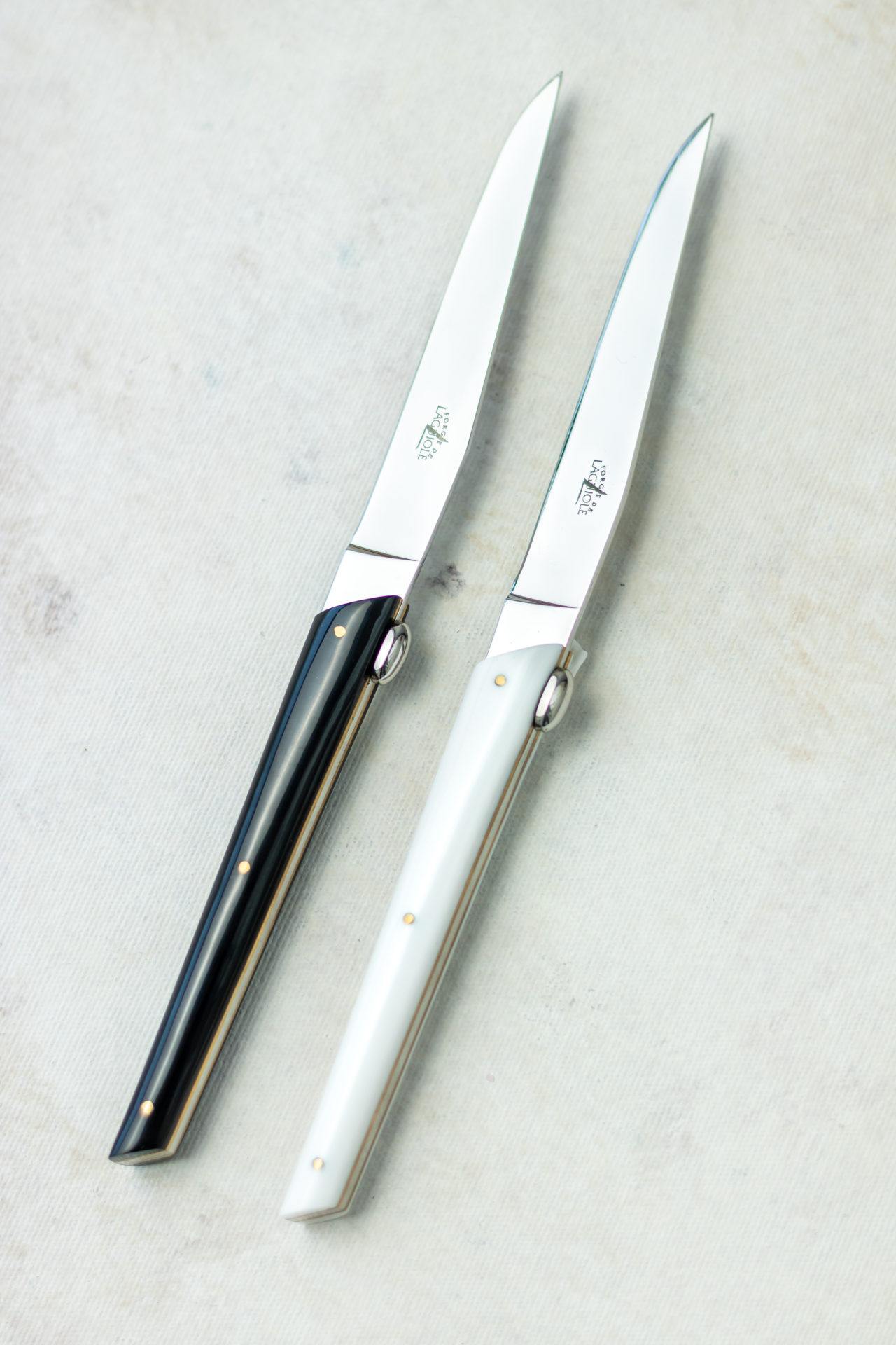 Laguiole Steakmesser Set, 2-teilig, mit schwarzen und weißen Griffen – Elegante Messer für die stilvolle Tischdekoration Zwei hochwertige Laguiole Steakmesser mit glänzenden Edelstahlklingen und Griffen in Schwarz und Weiß auf hellem Untergrund