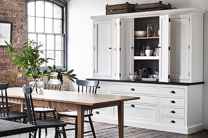 Moderne Landhausküche mit weißem Schrank, Holztisch und schwarzen Stühlen, stilvolle Einrichtungsidee Helle Küche im Landhausstil mit großem weißen Schrank, Holztisch, schwarzen Stühlen und dekorativen Elementen