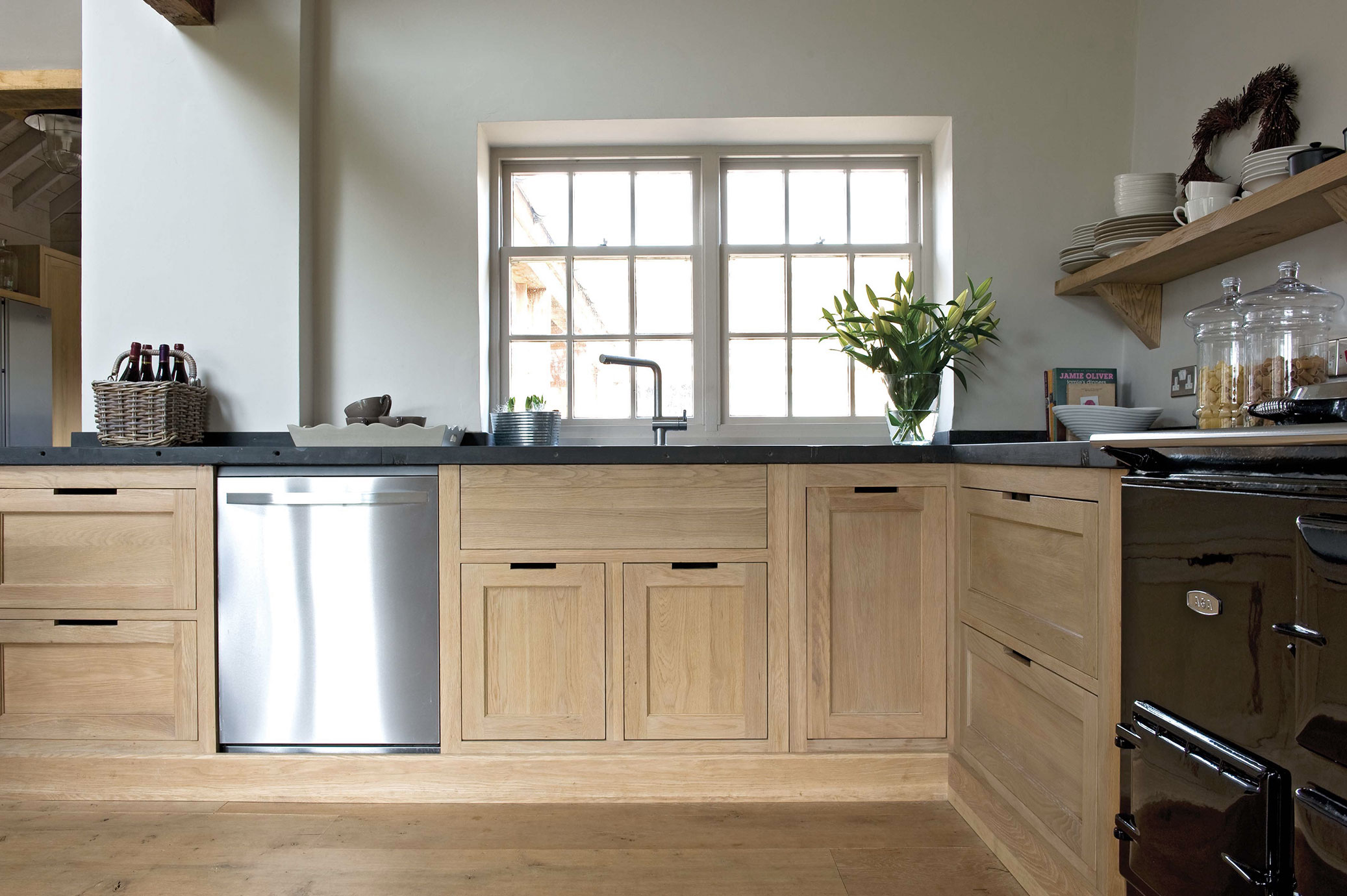 Moderne Landhausküche mit Holzfronten, Spülmaschine und Deko Helle Küche mit Fenster, Holzschränken, Spülmaschine, Arbeitsplatte, dekorativen Gläsern, Blumenstrauß und offenen Regalen