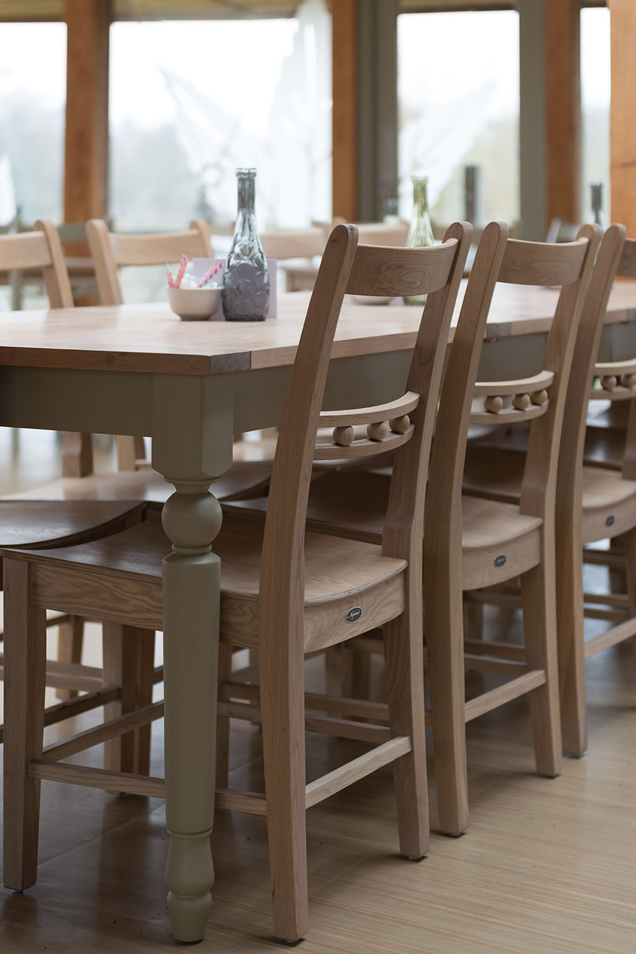 Massiver Esstisch aus Holz mit passenden Stühlen im modernen Esszimmer Holztisch mit klassischen Holzstühlen in einem hellen, modern eingerichteten Essbereich. Auf dem Tisch stehen Dekoflaschen und eine Schale.