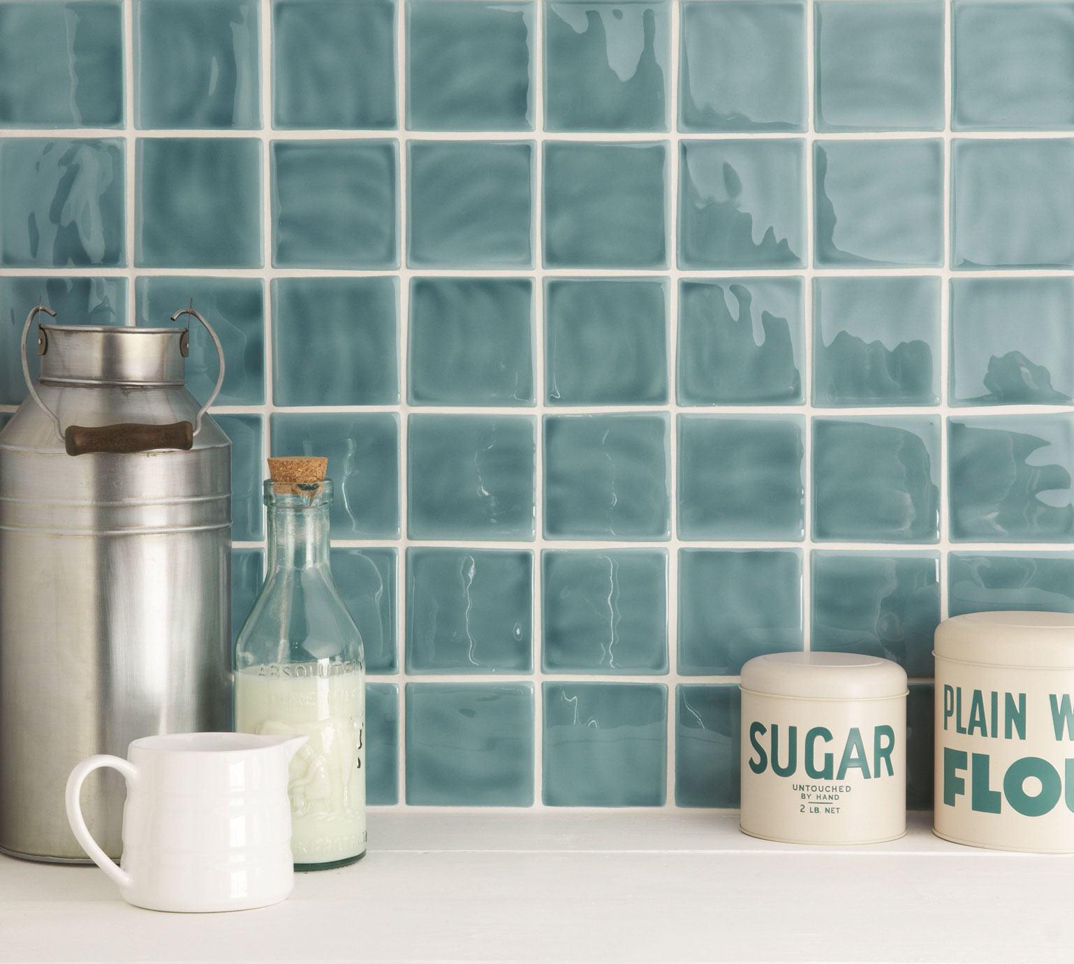 Glänzende blaue Küchenfliesen im Retro-Stil – Quadratische Wandfliesen als stilvoller Spritzschutz Detailansicht einer Küchenrückwand mit glänzenden, quadratischen, blauen Wandfliesen und dekorativen Vorratsbehältern für Zucker und Mehl