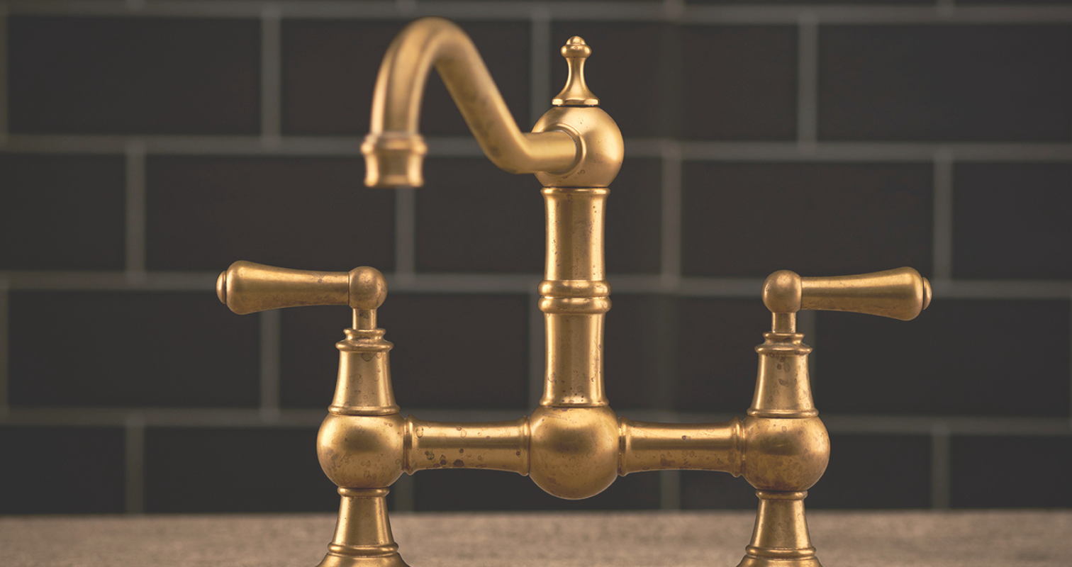 Messing-Wasserhahn im Vintage-Stil mit zwei Griffen für Waschbecken oder Küche Detailaufnahme eines goldfarbenen Messing-Wasserhahns im Retro-Design vor dunklem Fliesenhintergrund