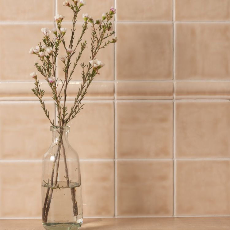 Glasvase mit Zweigen vor beigen Fliesen