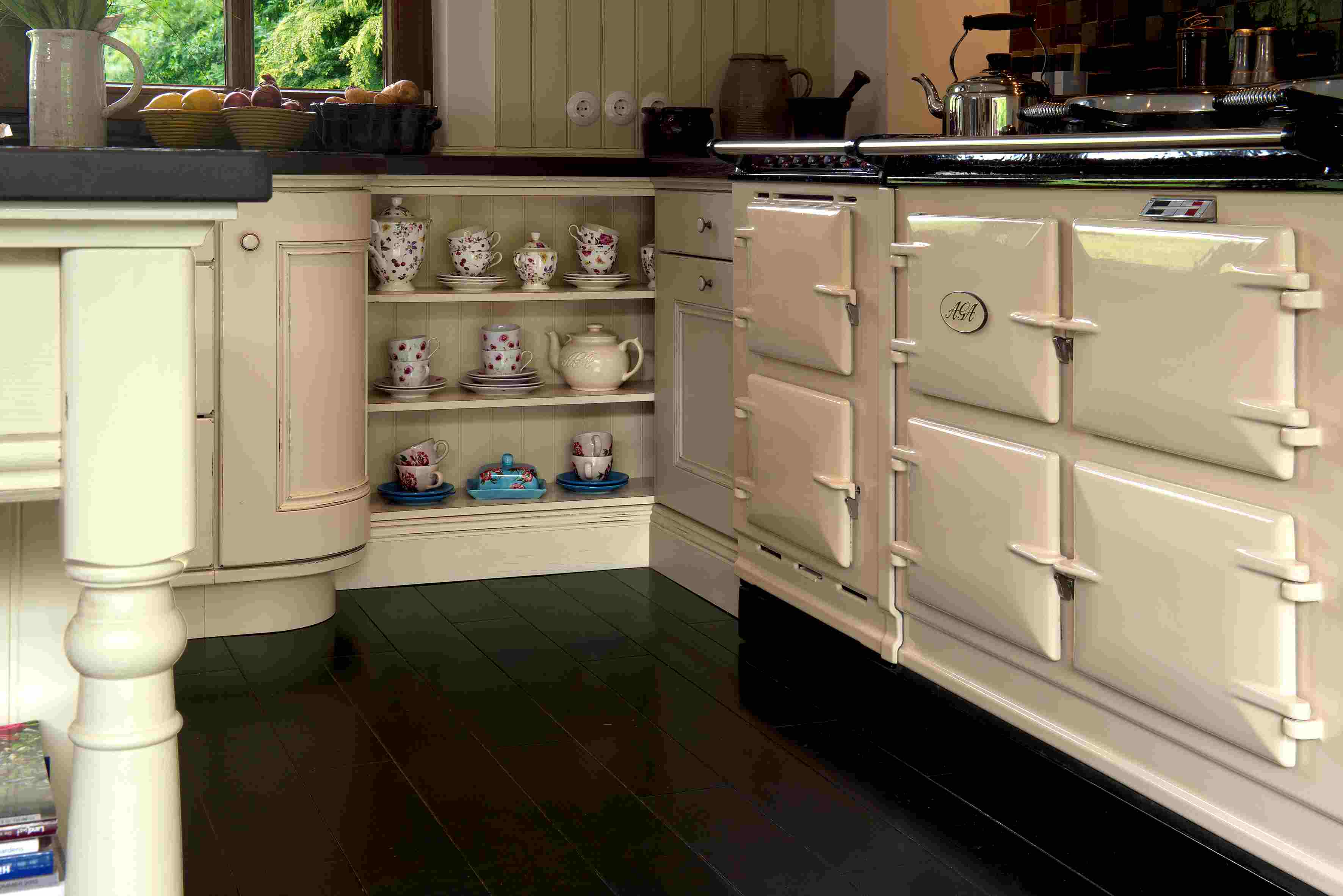 Traditioneller cremefarbener Küchenherd mit offenem Regal und Teeservice im Landhausstil Gemütliche Landhausküche mit cremefarbenem Ofen, offenem Regal mit Tassen und Teekanne sowie Obstschalen auf der Arbeitsplatte