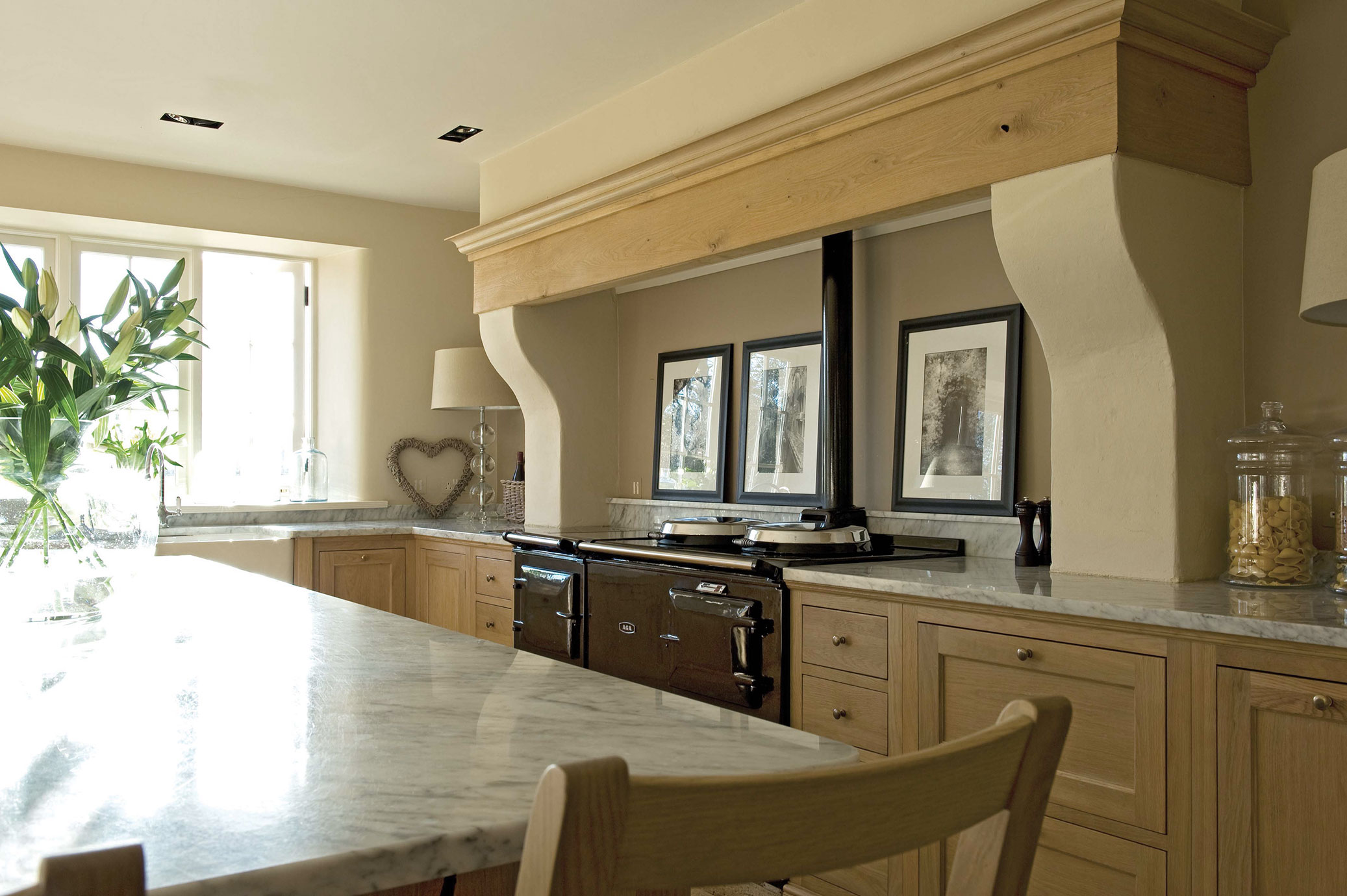 Moderne Landhausküche mit Naturstein-Arbeitsplatte und Holzfronten Helle Landhausküche mit großer Marmor-Arbeitsplatte, Holzunterschränken, schwarzem Herd, Fensterausblick und Dekoration.