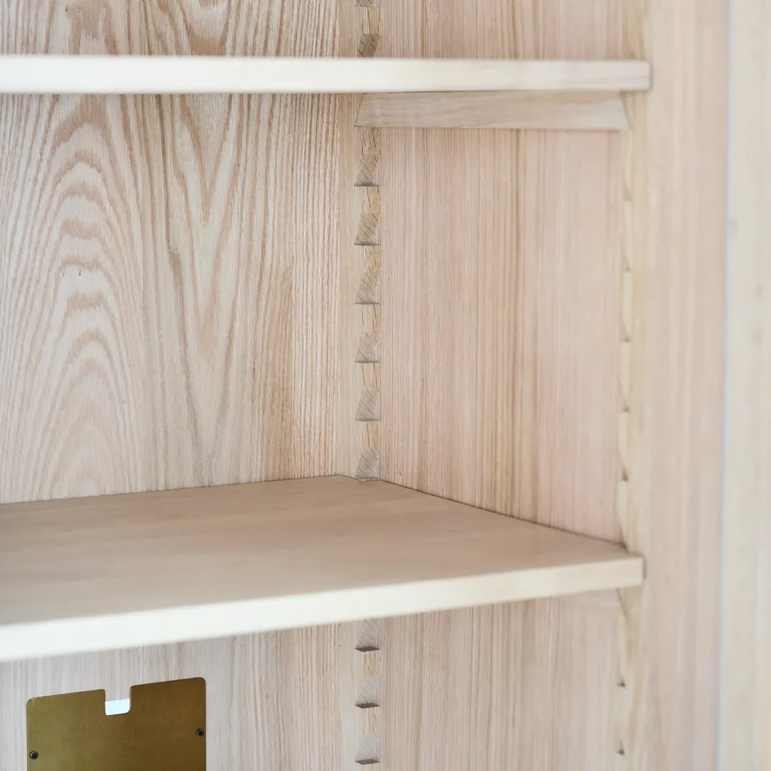 Detailfoto eines Schranks aus Holz mit höhenverstellbaren Einlegeböden und seitlicher Rasterleiste zur flexiblen Fachaufteilung