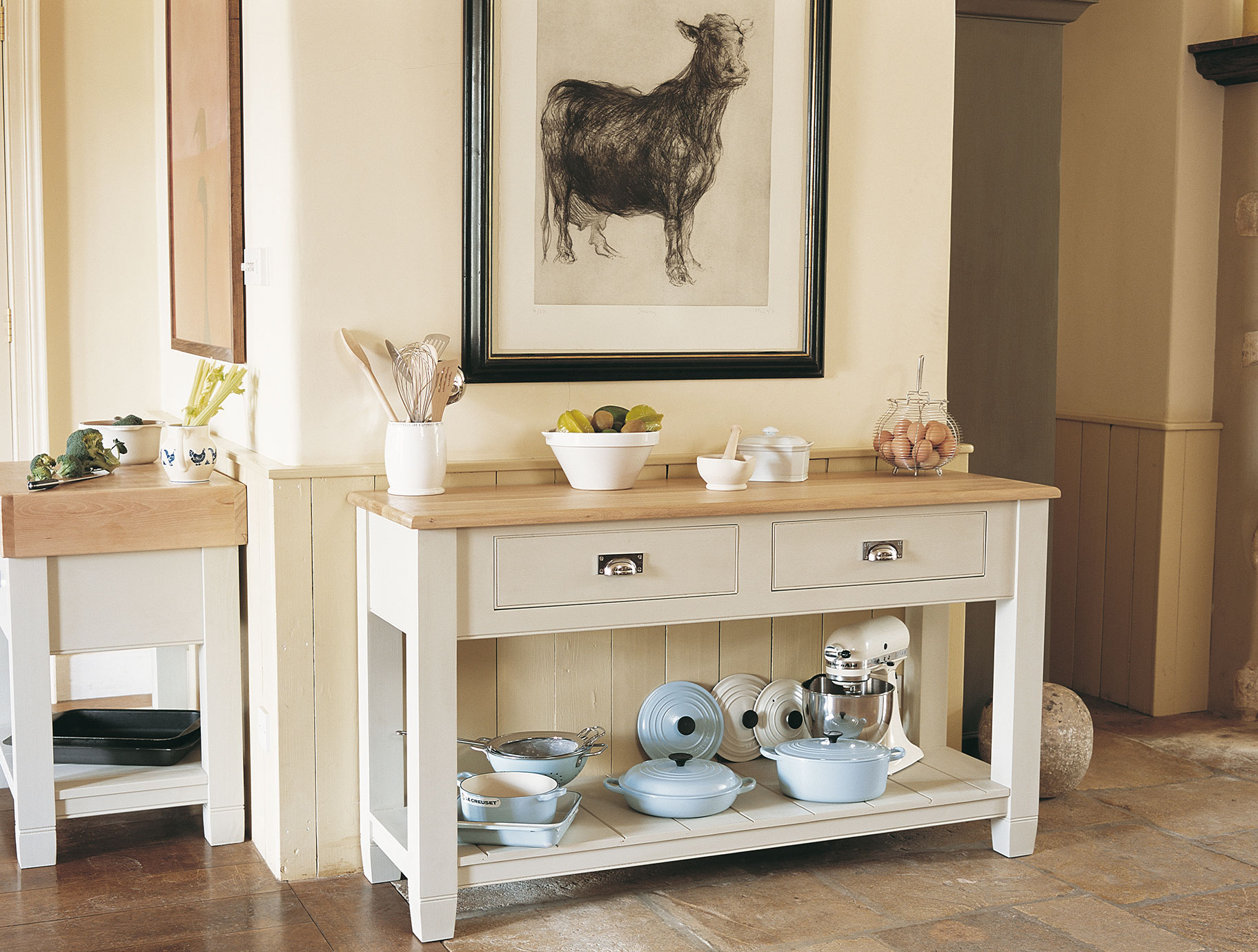 Landhausstil Küchenbuffet aus Holz mit verschiedenen Küchenutensilien und Kochgeschirr dekoriert Küchenbuffet im Landhausstil aus Holz mit Schubladen, darauf eine Schale mit Obst, ein Behälter mit Kochbesteck, eine Schale mit Eiern und weitere Küchenutensilien. Darunter befinden sich Töpfe, Schüsseln und eine Küchenmaschine.