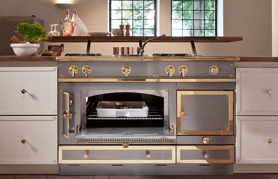 Luxuriöser Herd mit goldenen Akzenten in moderner Landhausküche, Ofen geöffnet mit Bratform Eleganter Herd mit goldfarbenen Details und offenem Backofen, der eine Auflaufform enthält, eingebaut in einer hochwertigen Küche