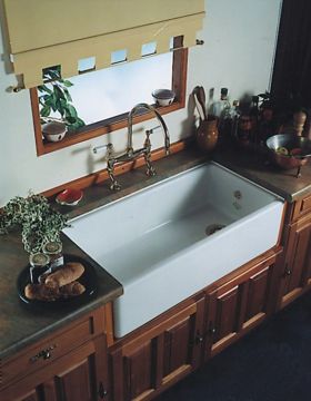 Rustikale Küchenspüle aus Keramik mit Landhausstil-Holzunterschrank und Armatur vor Fenster Weiße, große Keramikspüle im Landhausstil mit Messingarmatur, Holzunterschränken und Küchenaccessoires vor einem Fenster