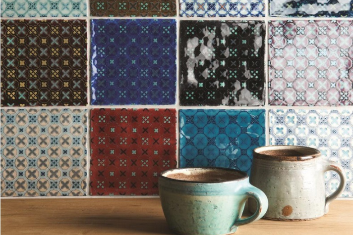Zwei Keramiktassen mit Kakao vor bunter Fliesenwand im Vintage-Muster Zwei handgefertigte Tassen gefüllt mit Kakao stehen auf einem Holztisch vor einer Wand aus bunten, gemusterten Fliesen im Retro-Stil.